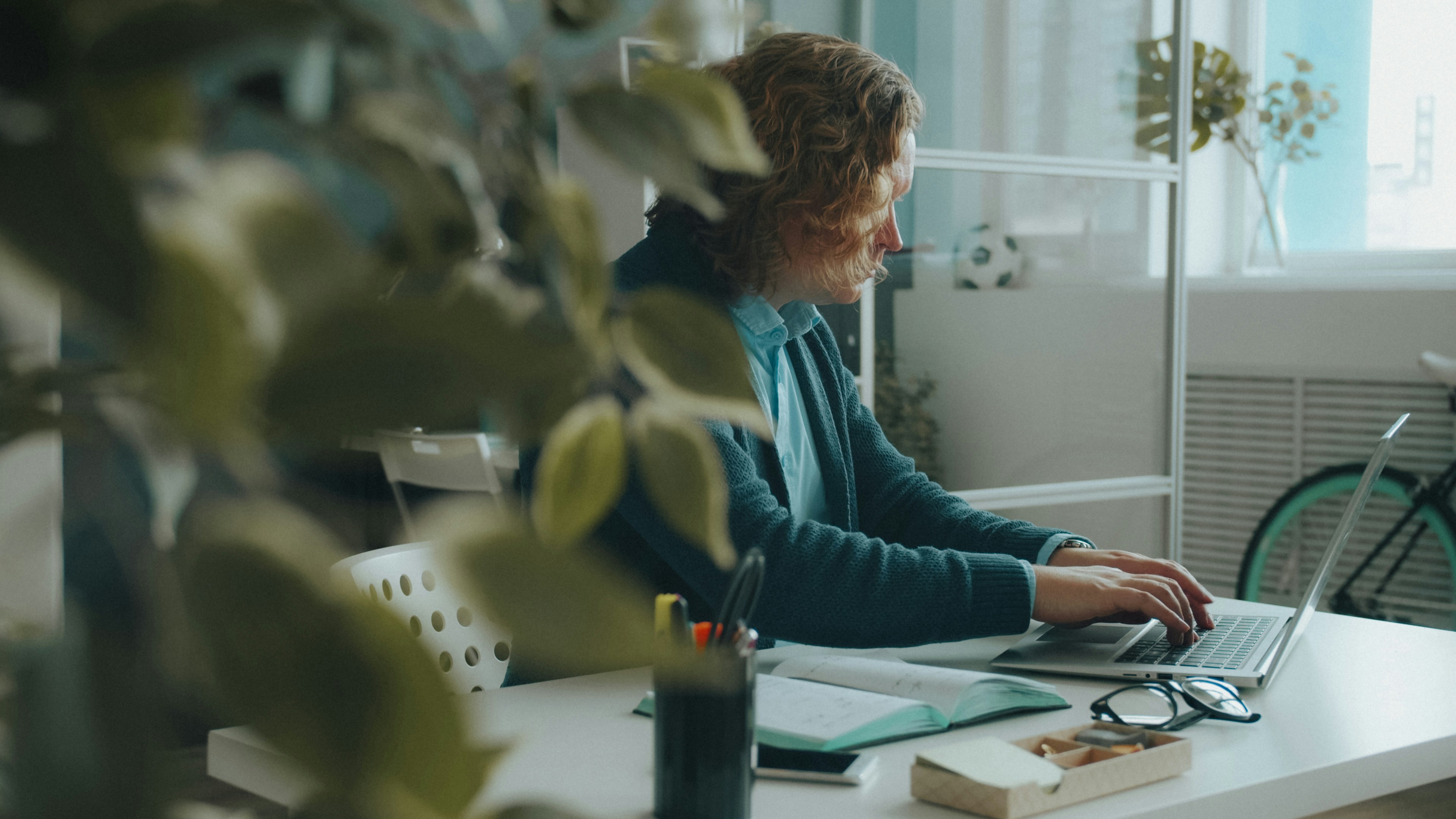 person working at laptop in home office - A person with curly hair typing on a laptop at a white desk