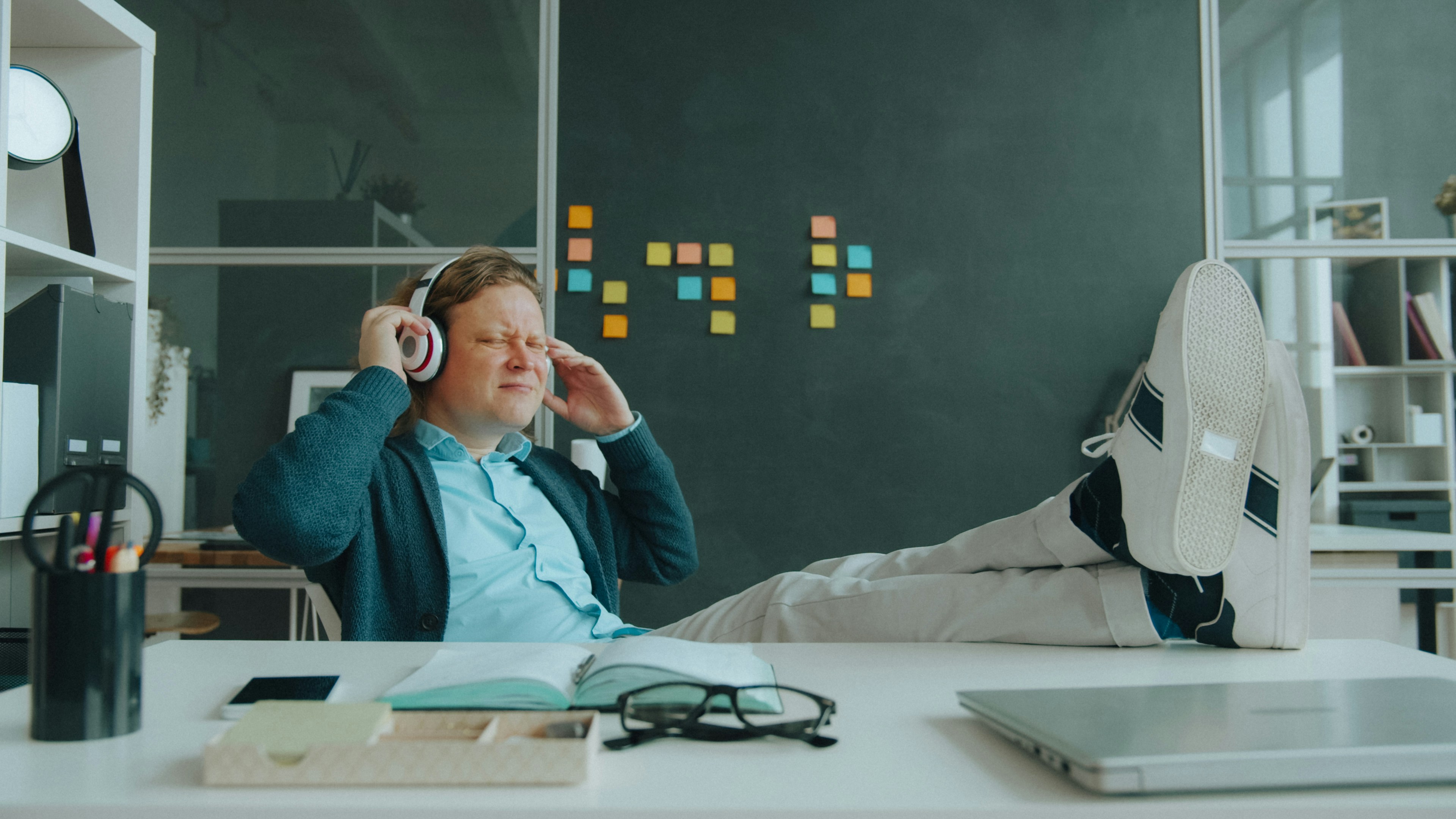 A person with headphones relaxing with feet on a desk in a workspace