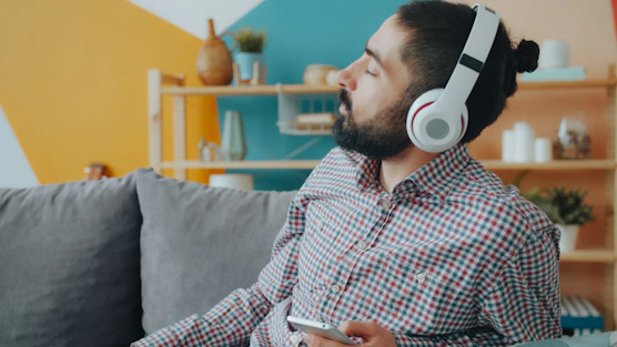 A man wearing white headphones in a plaid shirt on a grey sofa