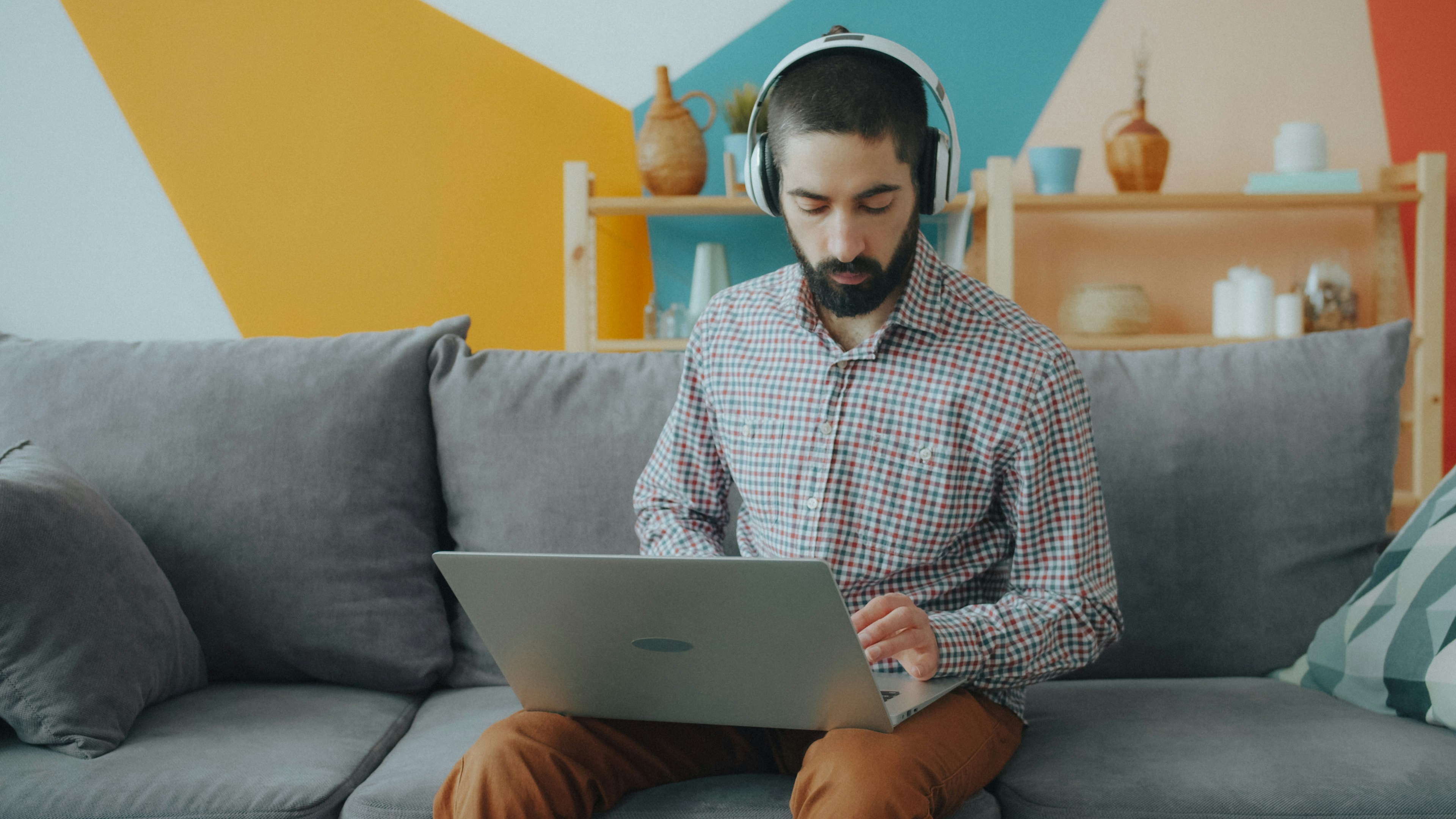 Man in headphones working on a laptop on a grey couch