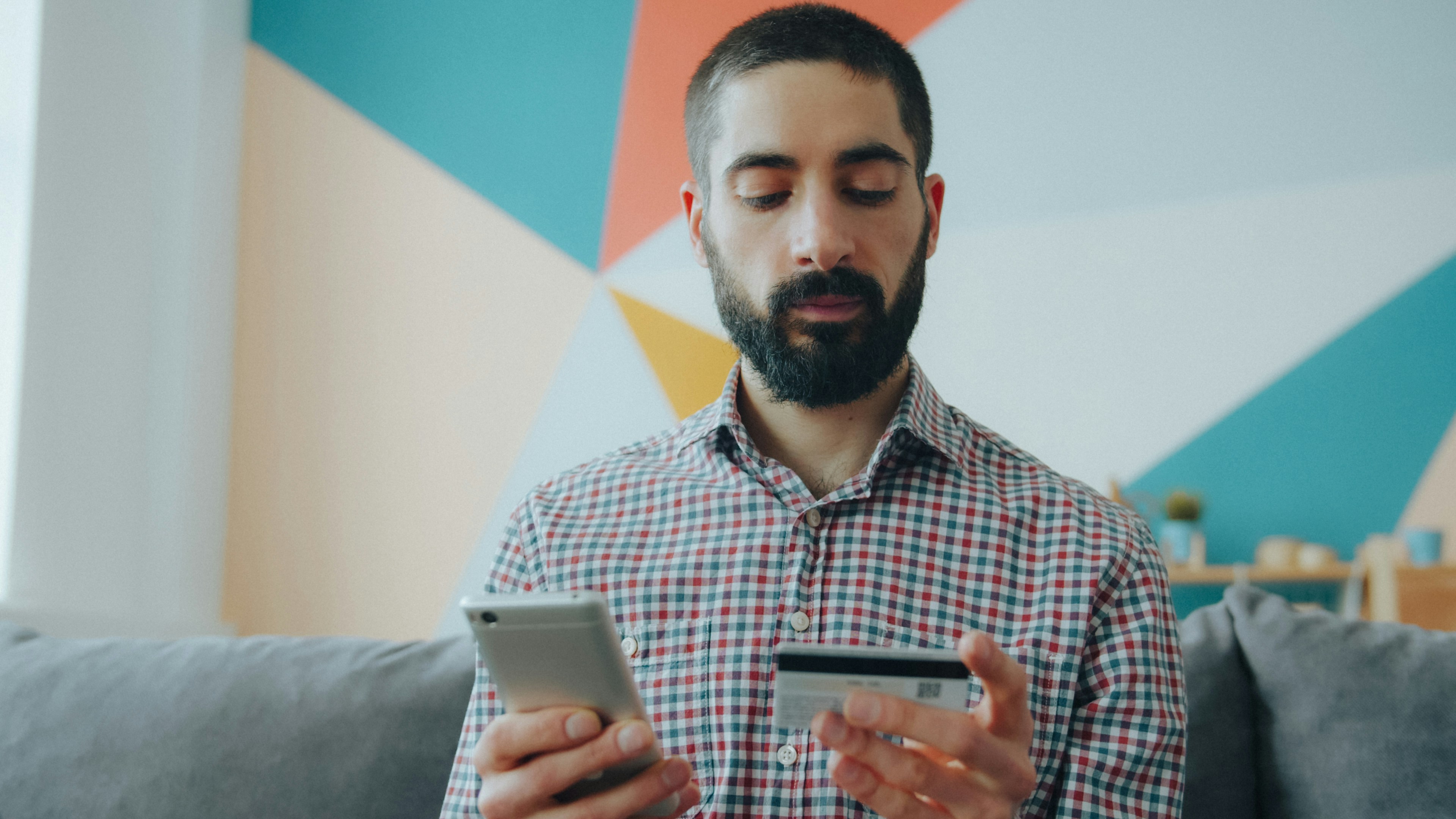 A man in a plaid shirt holding a smartphone and a credit card