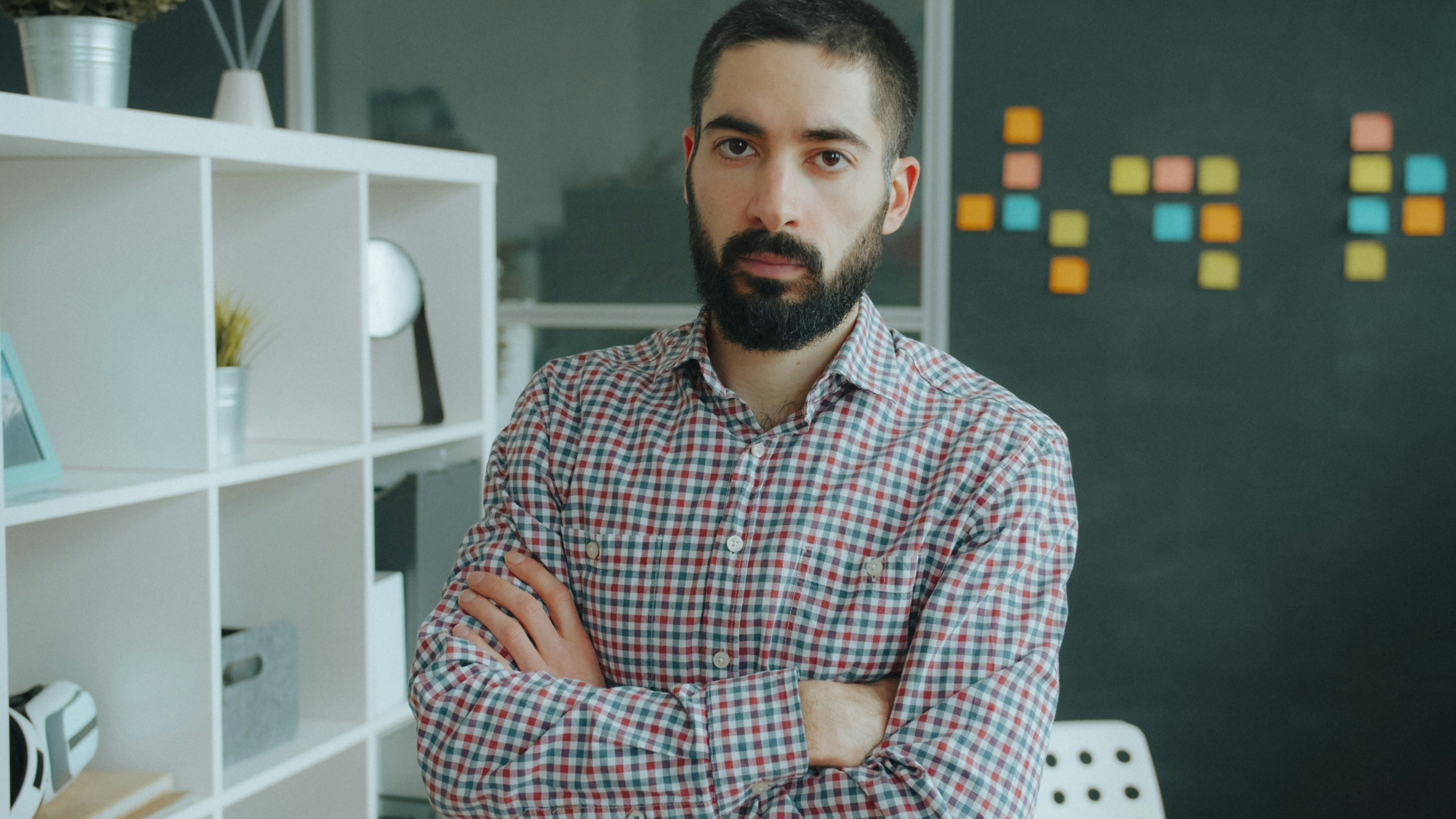 A man with a beard in a plaid shirt standing in a workspace