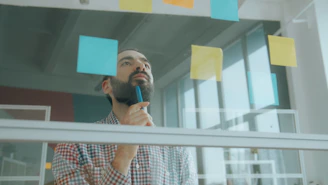 A man in a plaid shirt looking at sticky notes on a glass wall