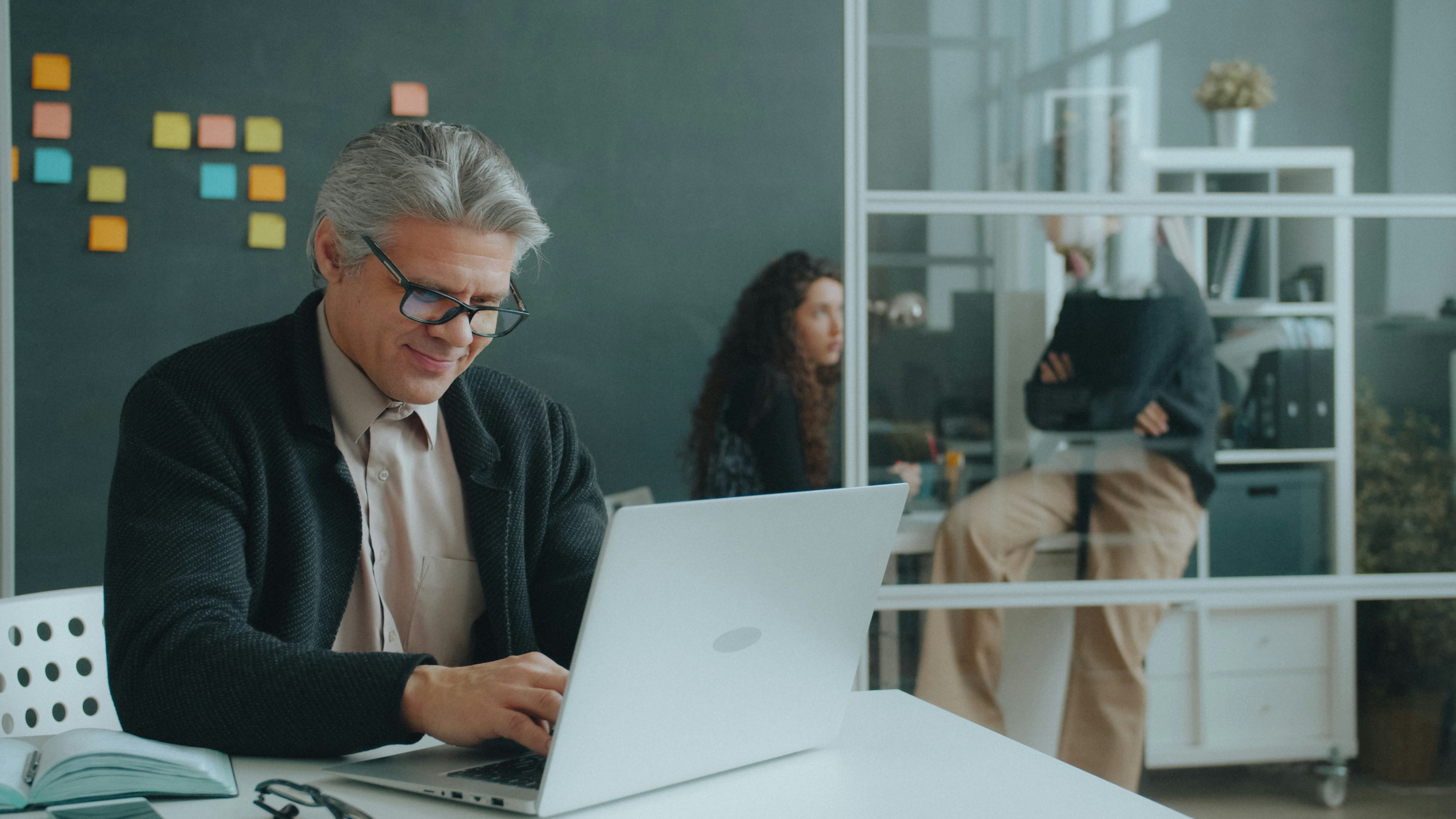 A man with grey hair typing on a laptop in a modern office