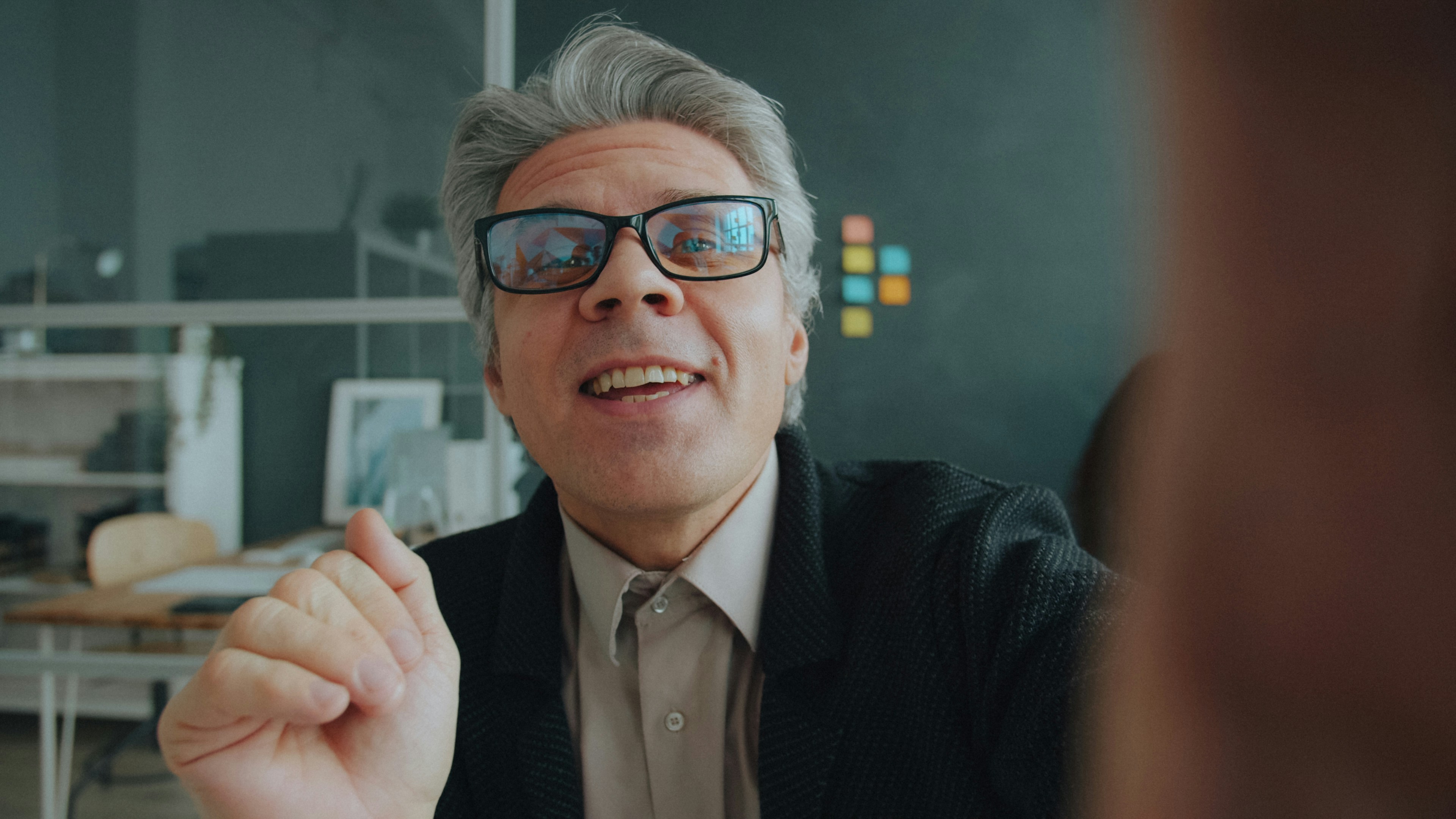 A man with grey hair and glasses talking in a modern office workspace