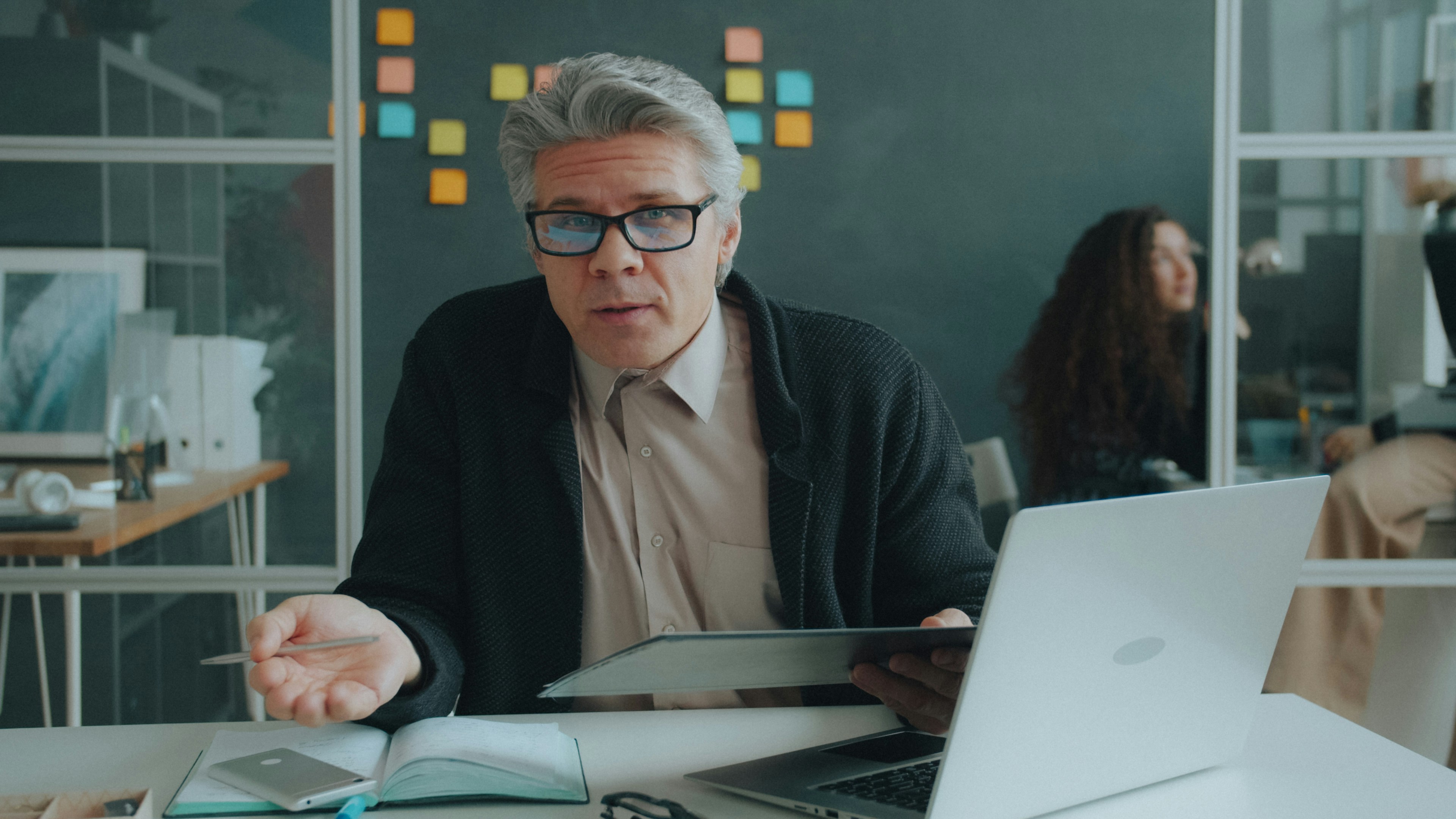 Grey-haired man gesturing at a laptop in an office