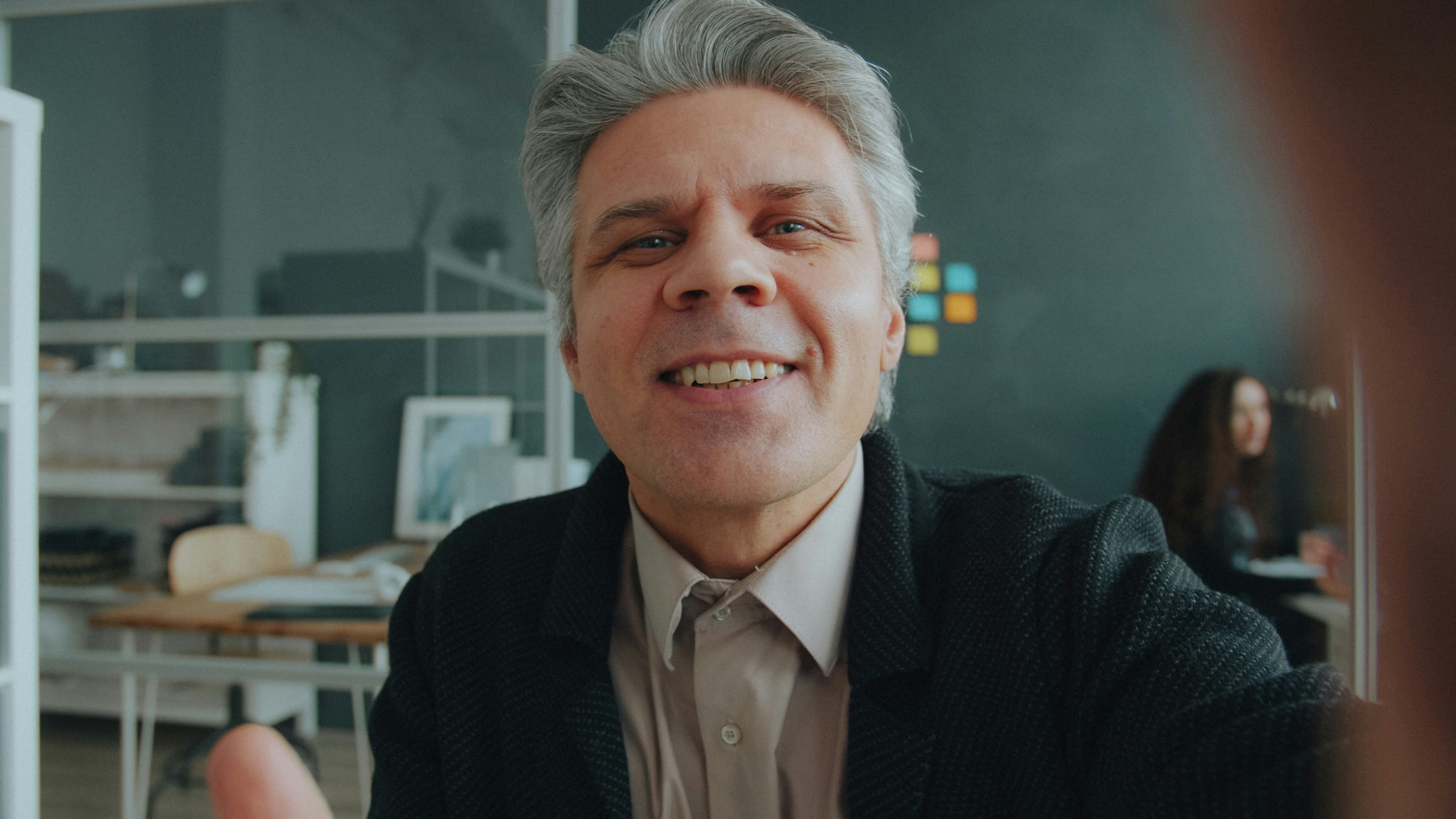 A man with grey hair smiling during a video call in an office