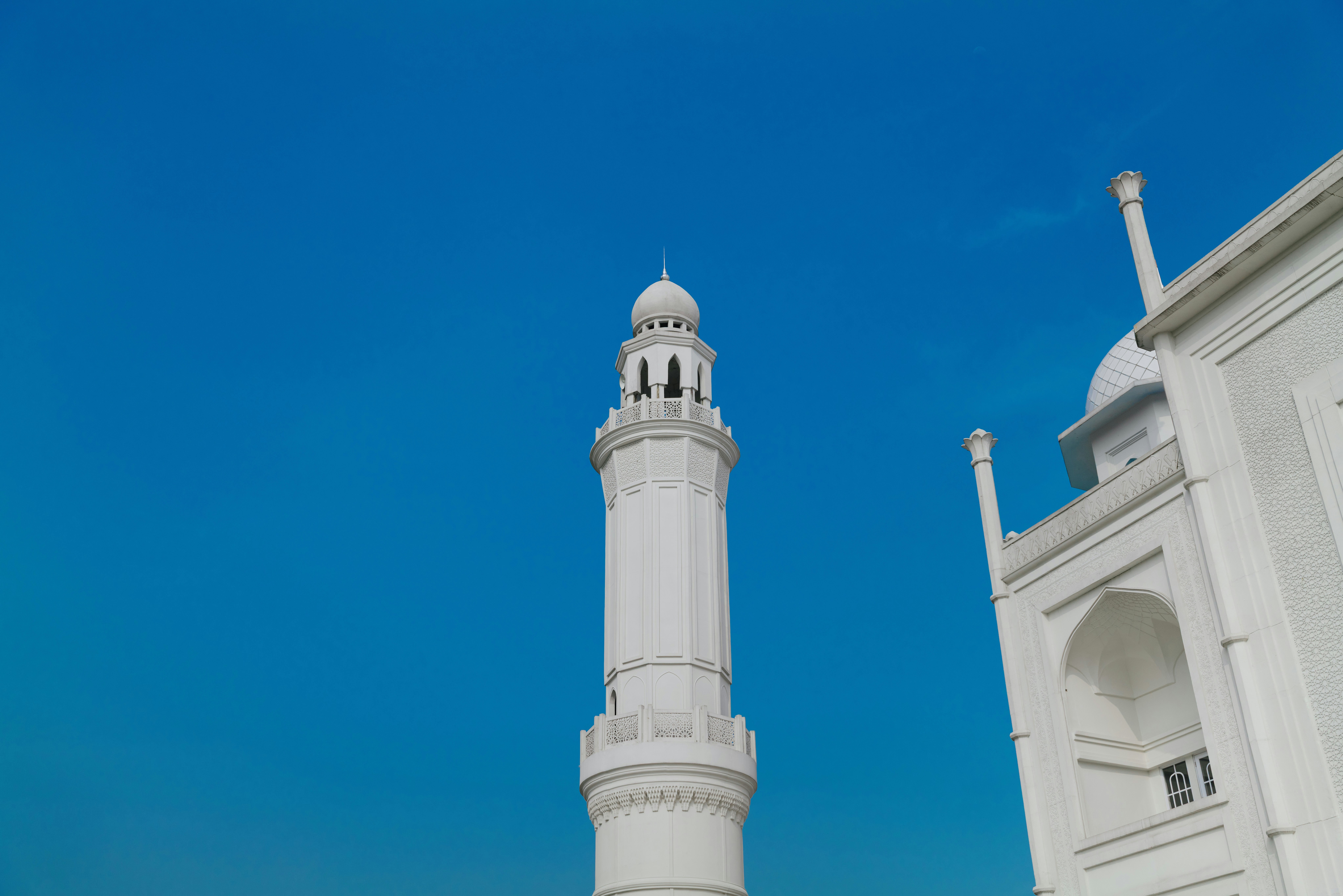 A white minaret beside the carved corner of Masjid Budi Guna in Bogor