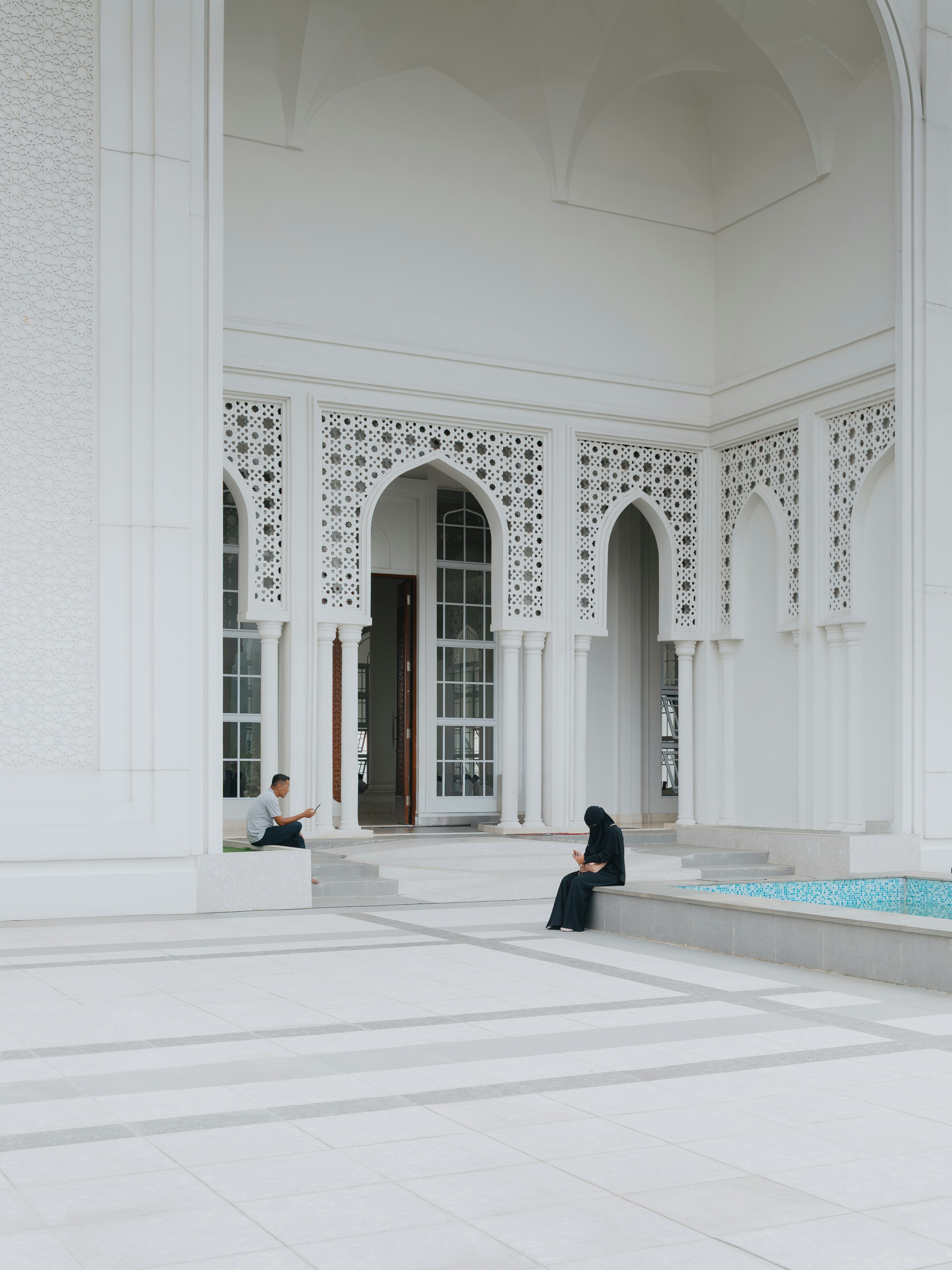 Due persone sedute nel cortile di una moschea bianca con intricati schermi intagliati