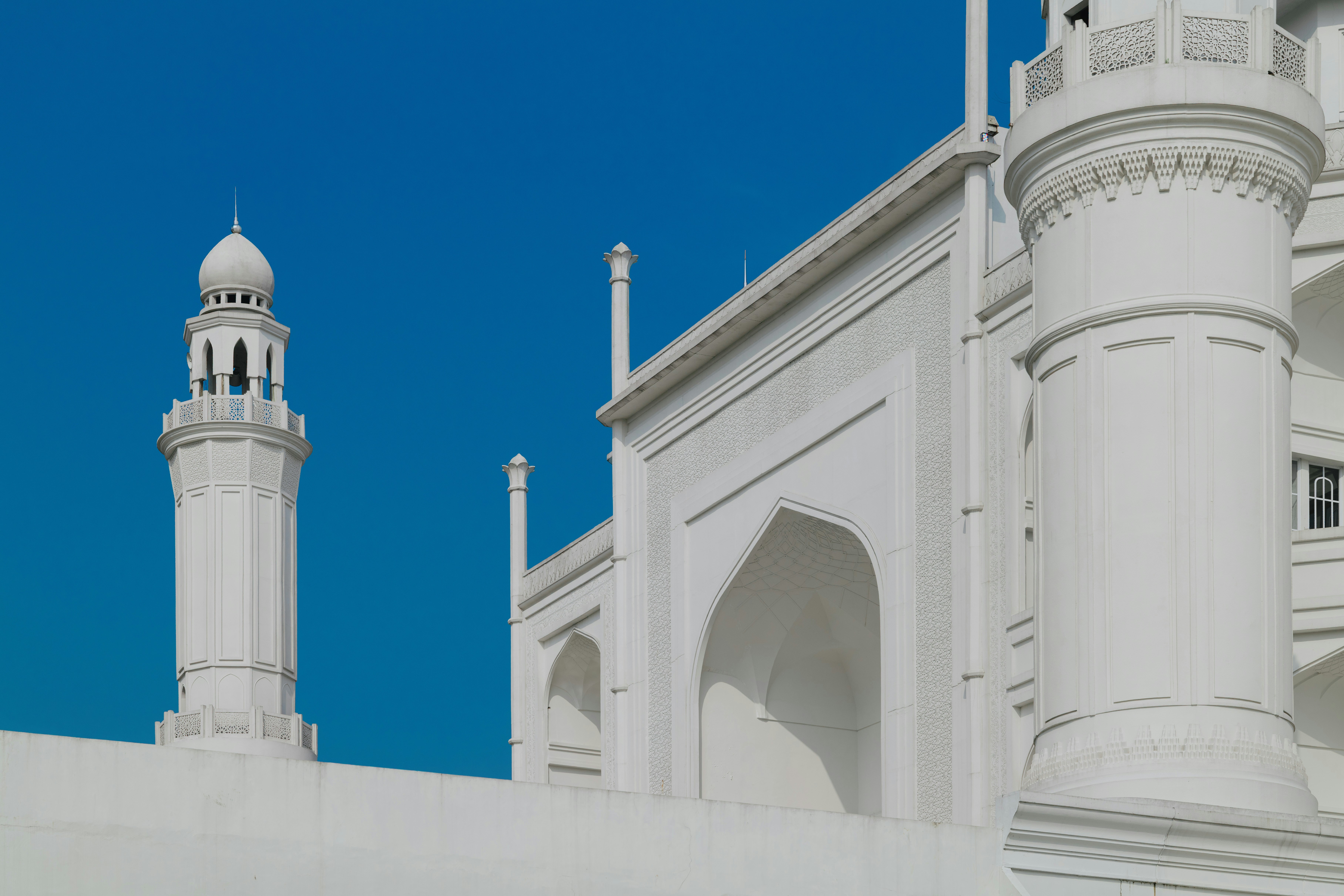 A white minaret and carved walls of Masjid Budi Guna in Bogor against blue sky