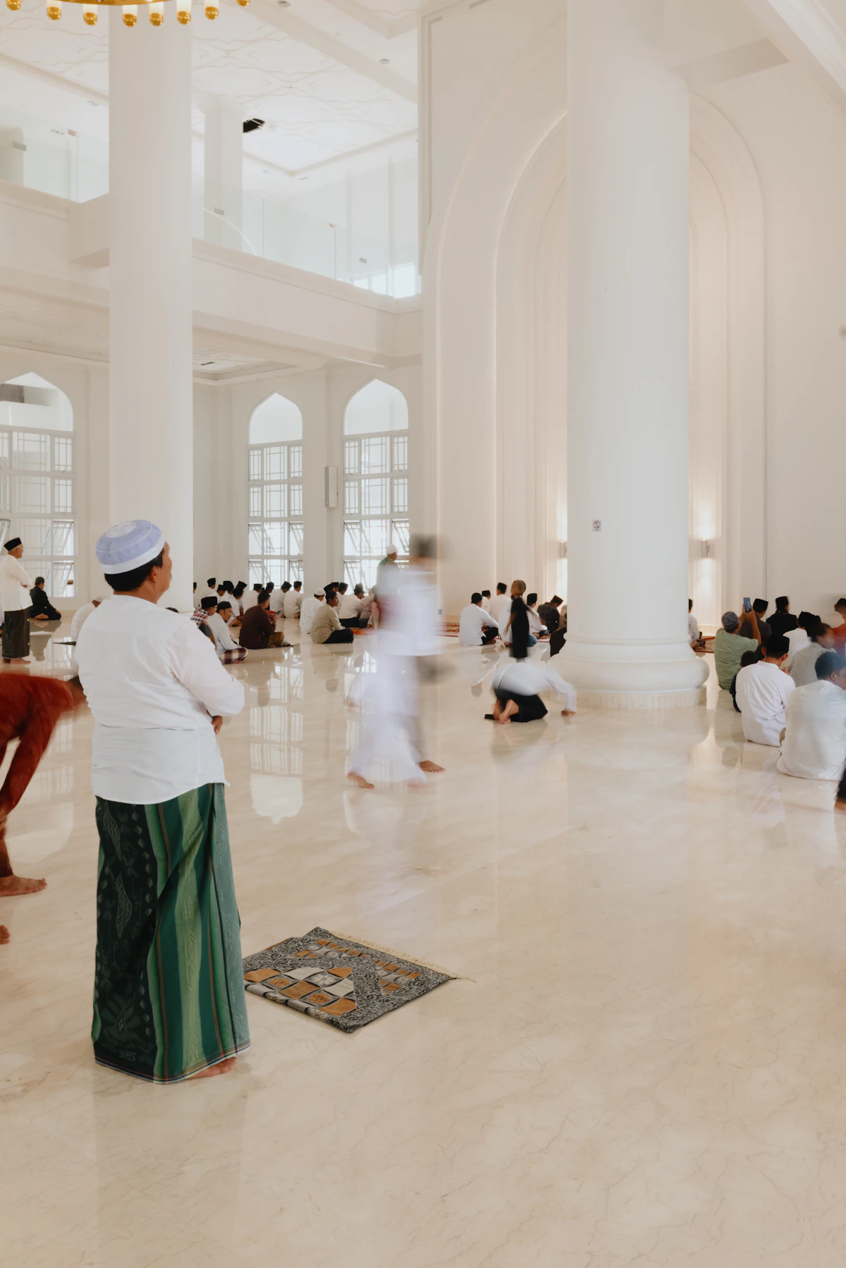 Seorang pria berjalan di ruang salat masjid yang putih terang