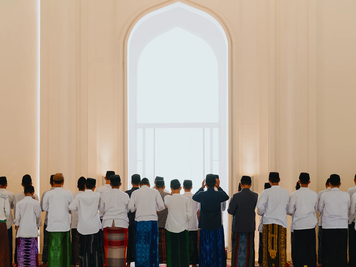 Jamaah laki-laki salat berbaris di depan jendela lengkung masjid