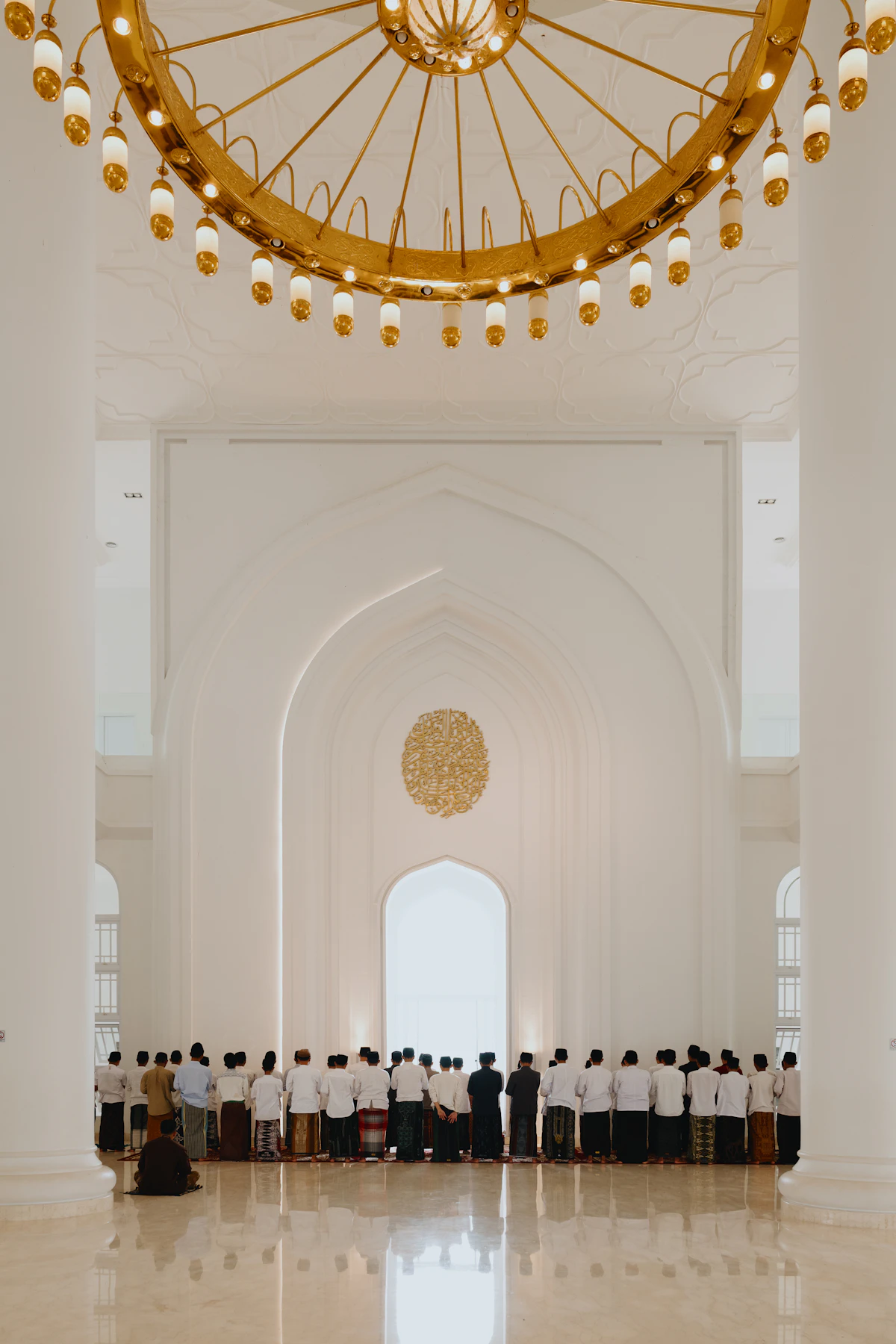 Jamaah salat di bawah lampu gantung emas dalam masjid