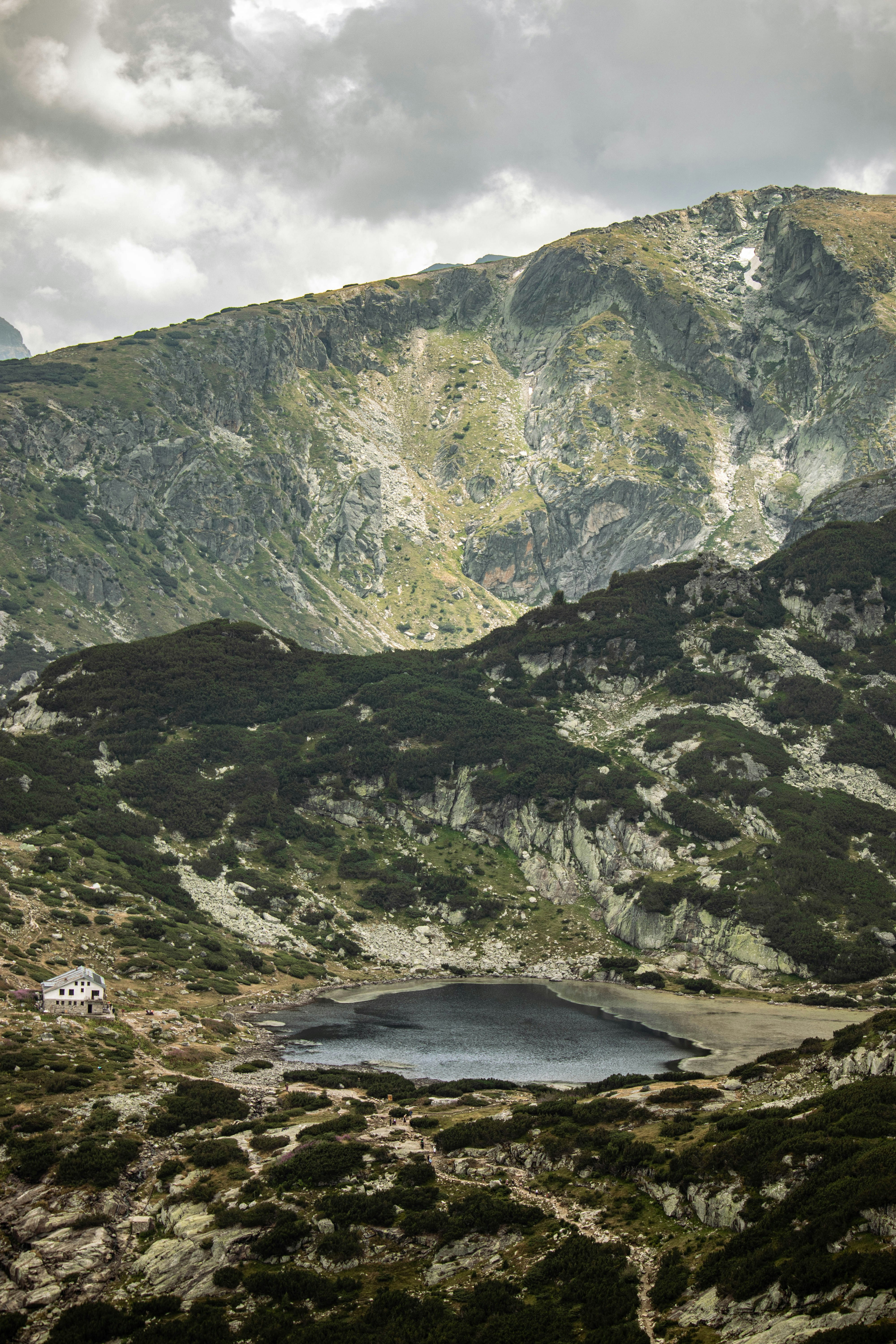A small stone cabin beside a dark mountain lake under a cloudy sky