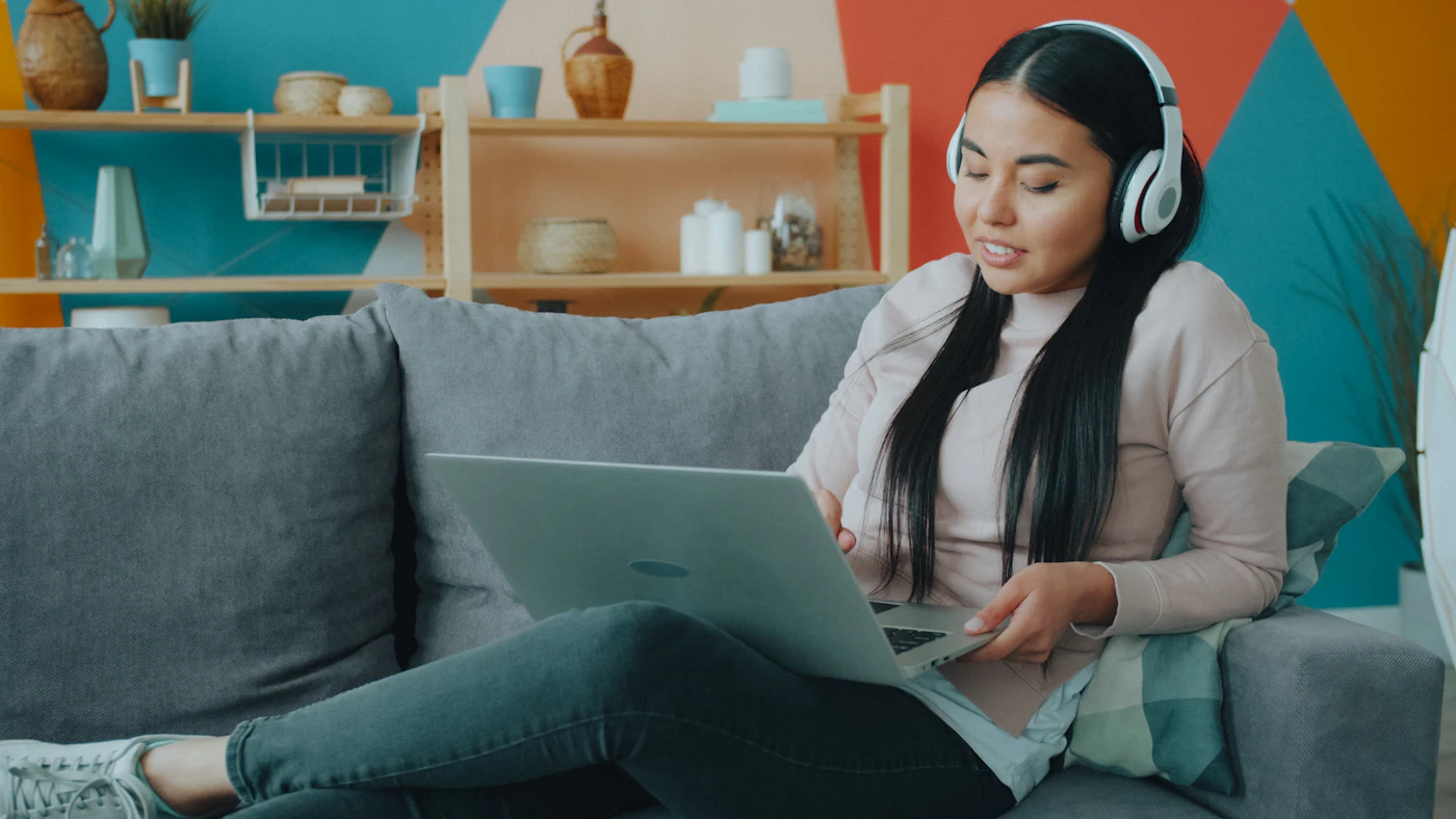 Woman with headphones working on a laptop on her couch