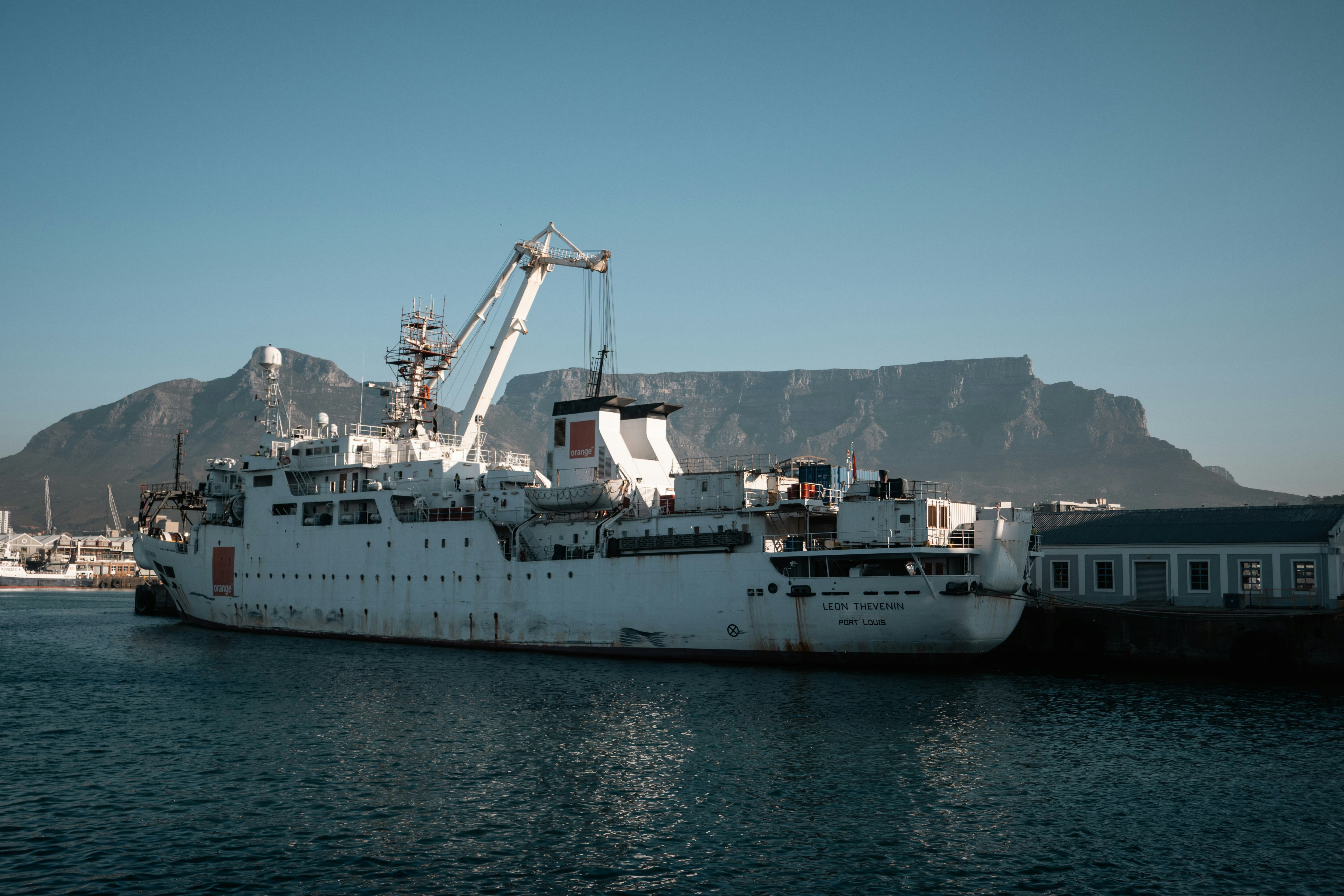 A white cable ship docked at a harbor with Table Mountain in Cape Town