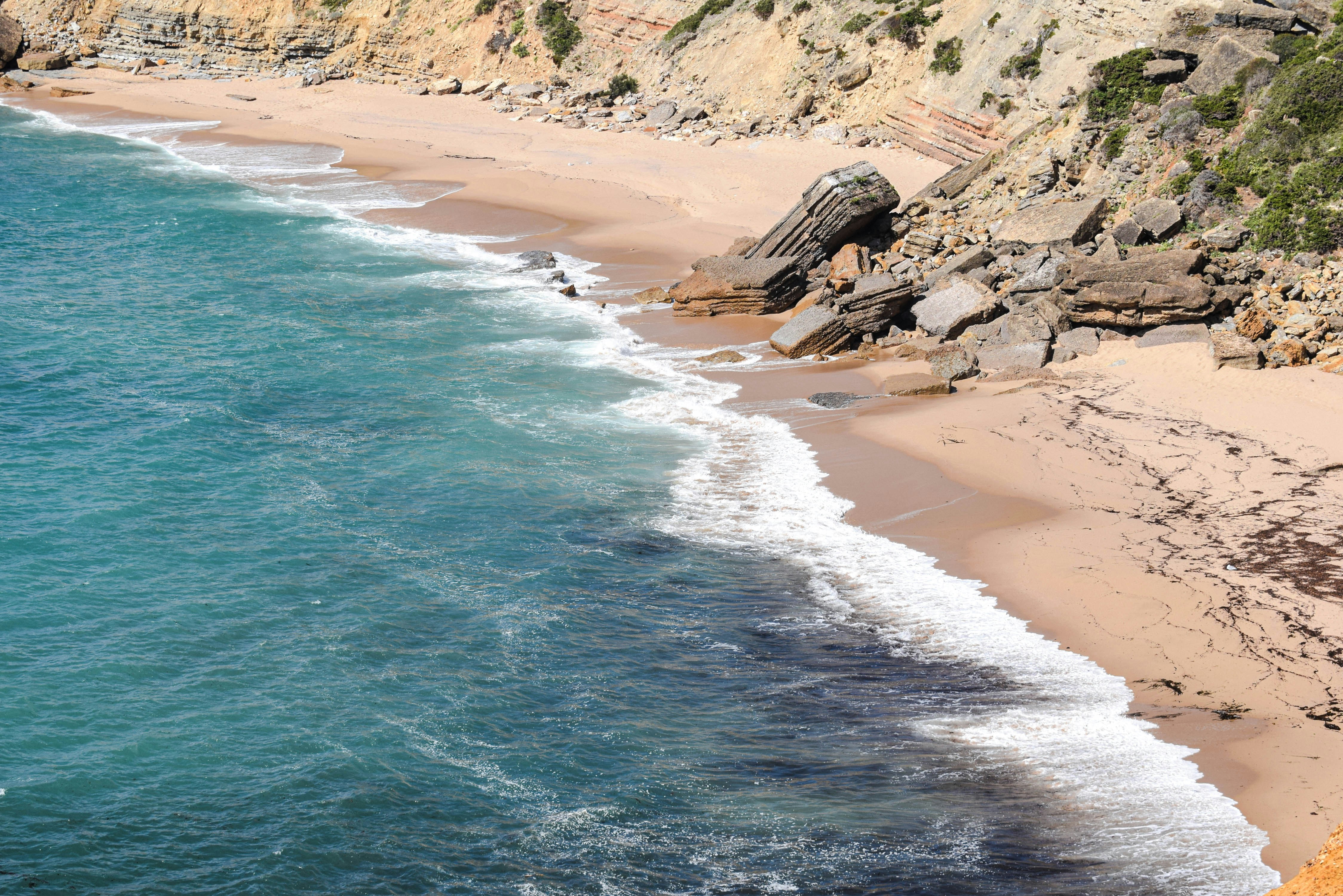 Turquoise waves washing onto a sandy beach below a rocky cliffside