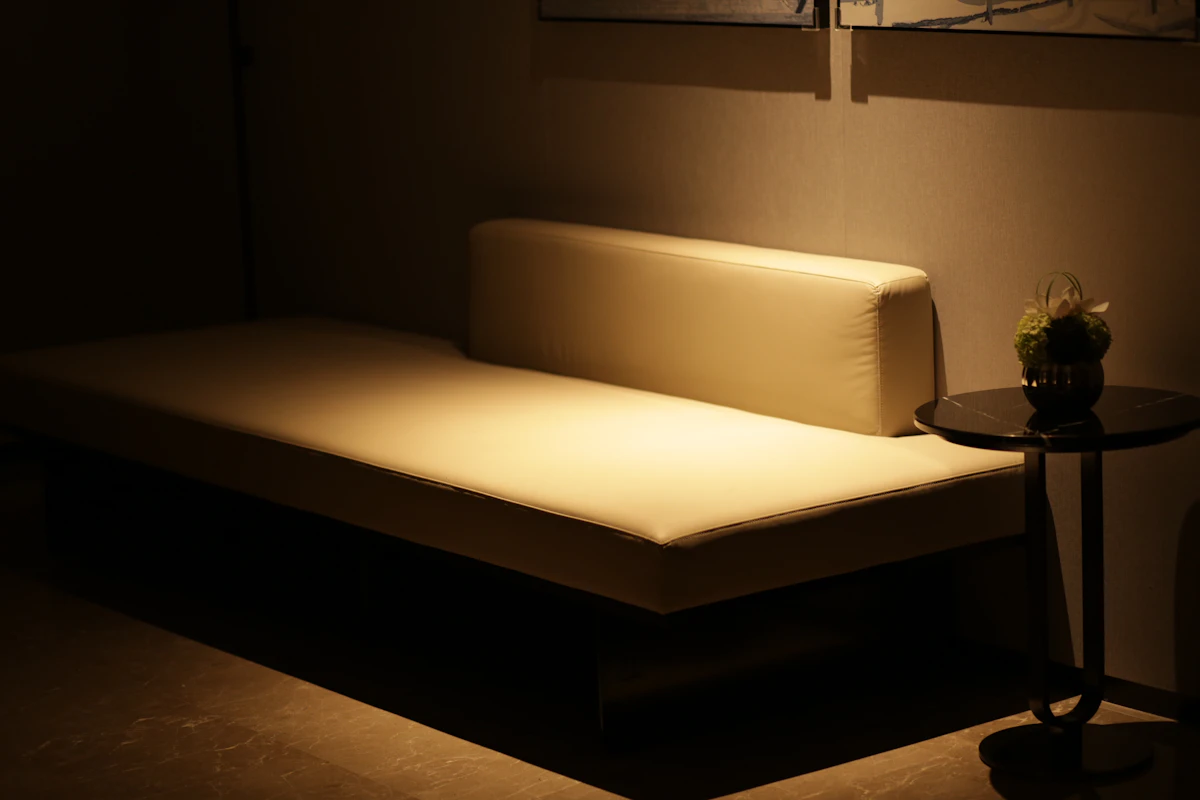 A cream daybed and a small side table lit by a single warm lamp