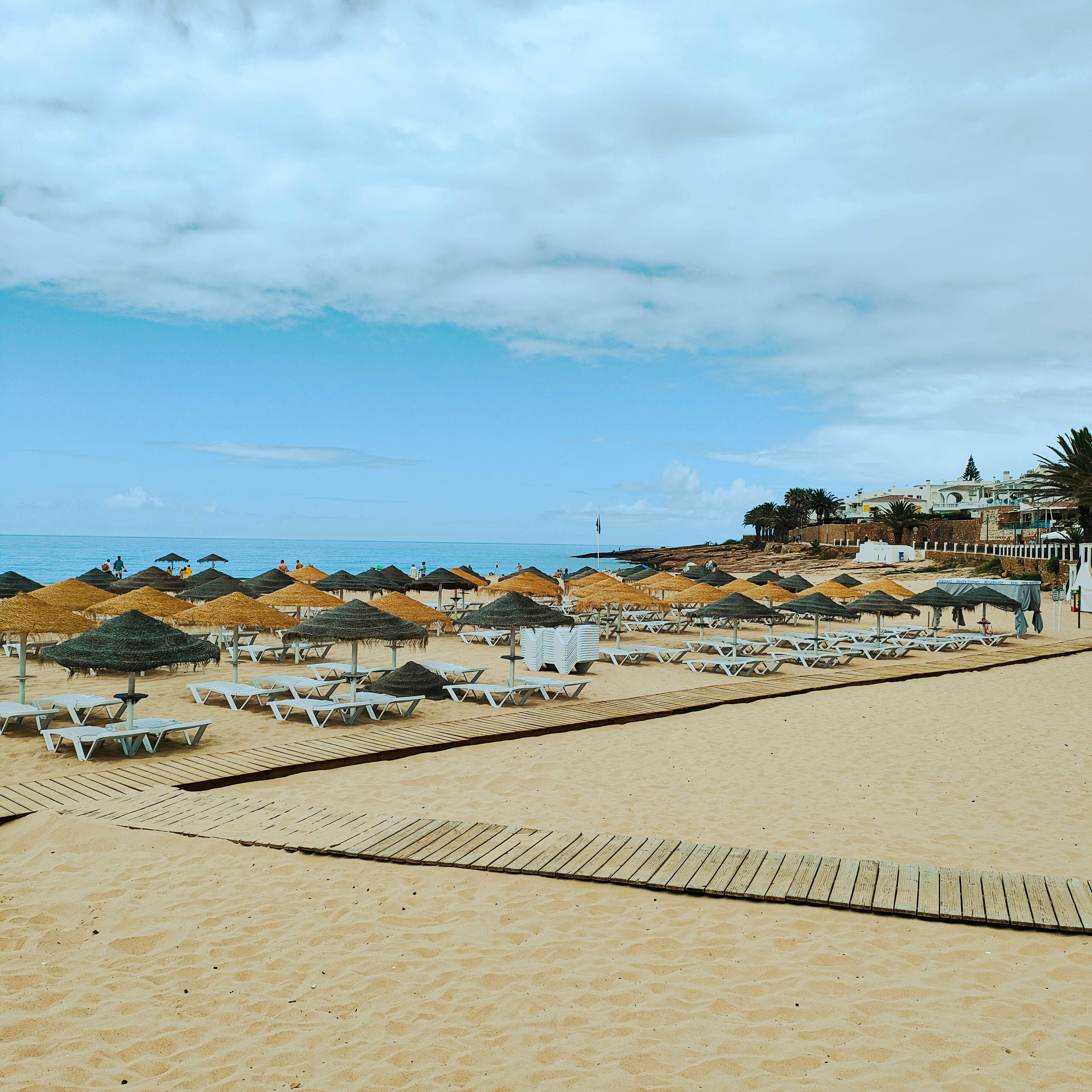 Straw umbrellas and white lounge chairs on a sandy beach under a cloudy sky