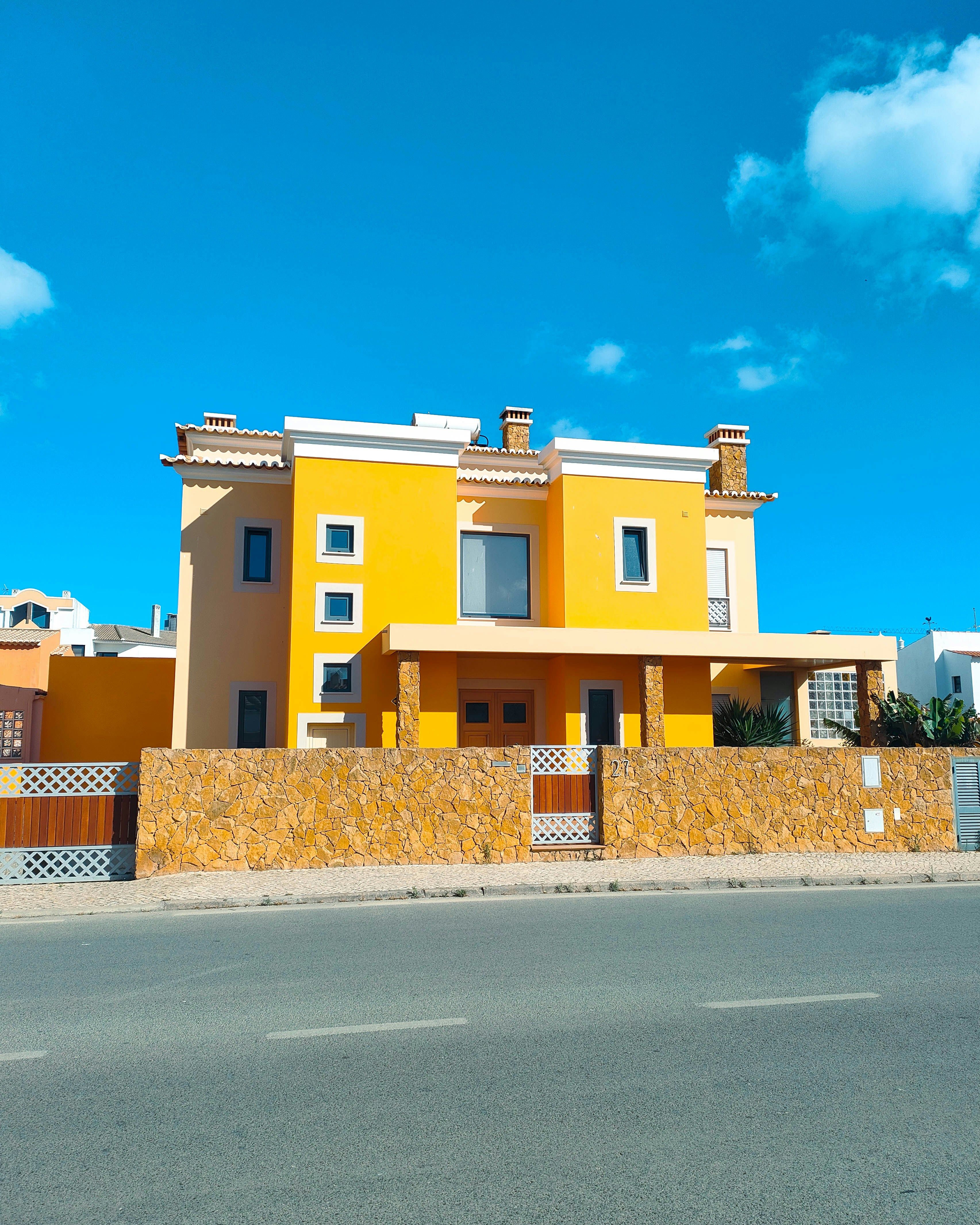 A bright yellow house with a stone wall behind a paved road