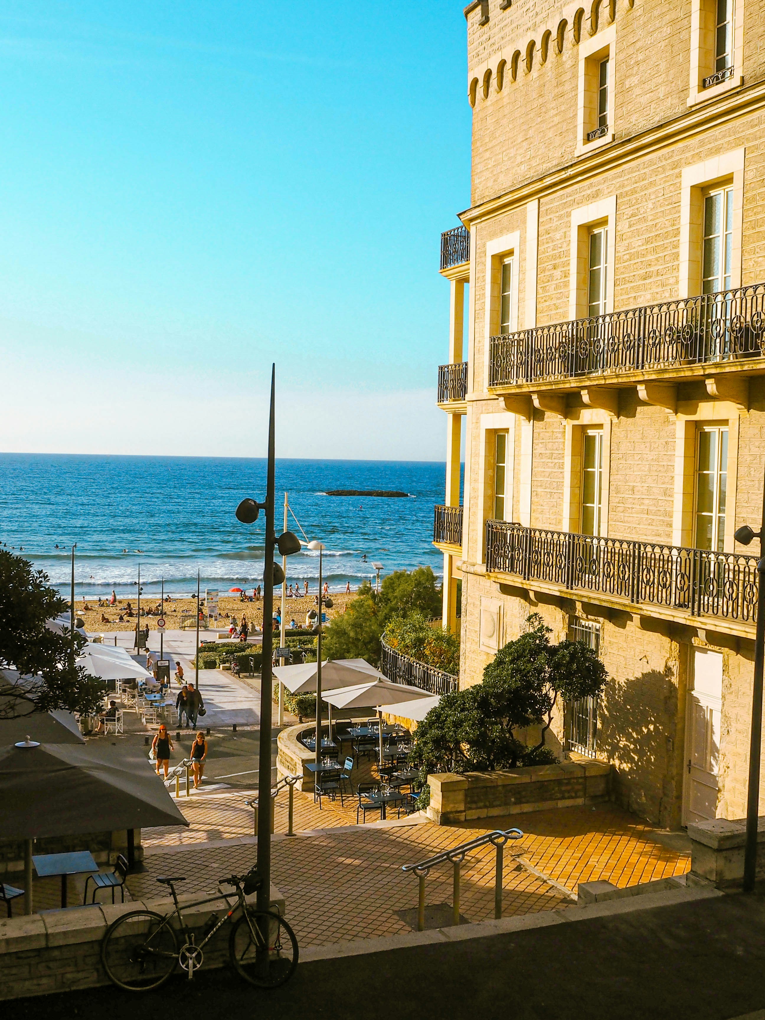 A stone building with balconies overlooking a sandy beach and the blue ocean