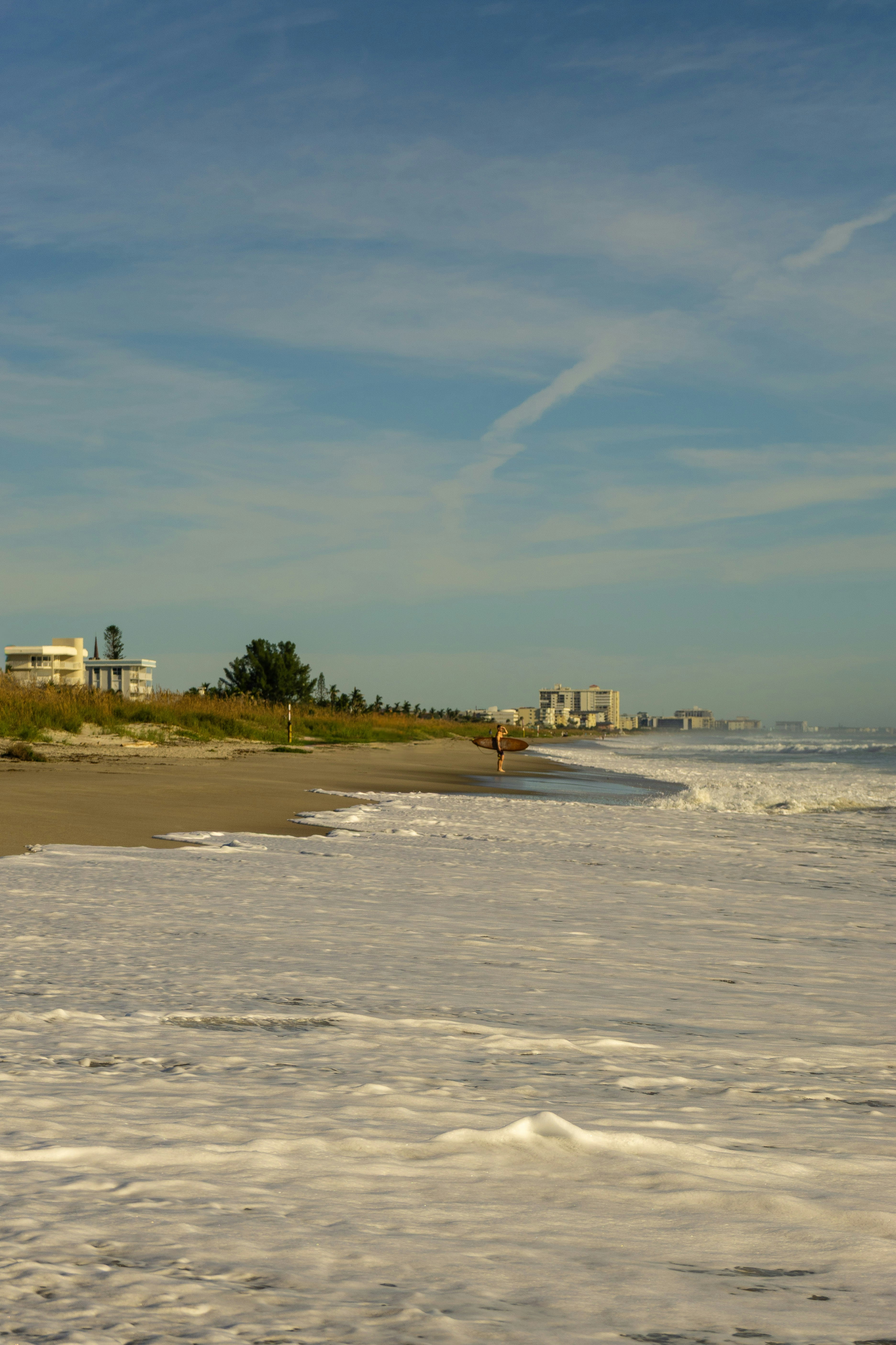 A person holding a surfboard on a sandy beach with foamy waves