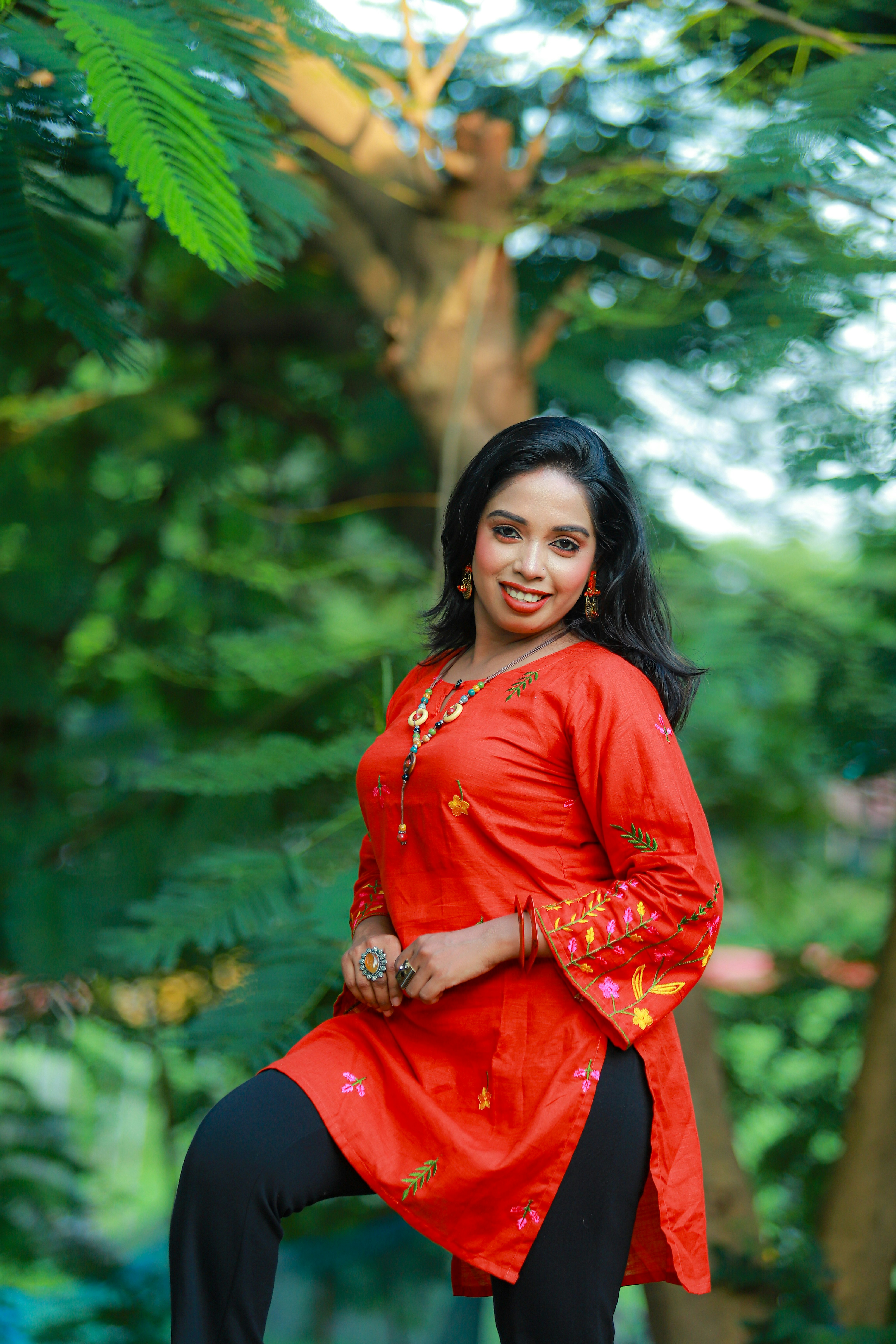 A woman in a red embroidered tunic and black pants in a garden