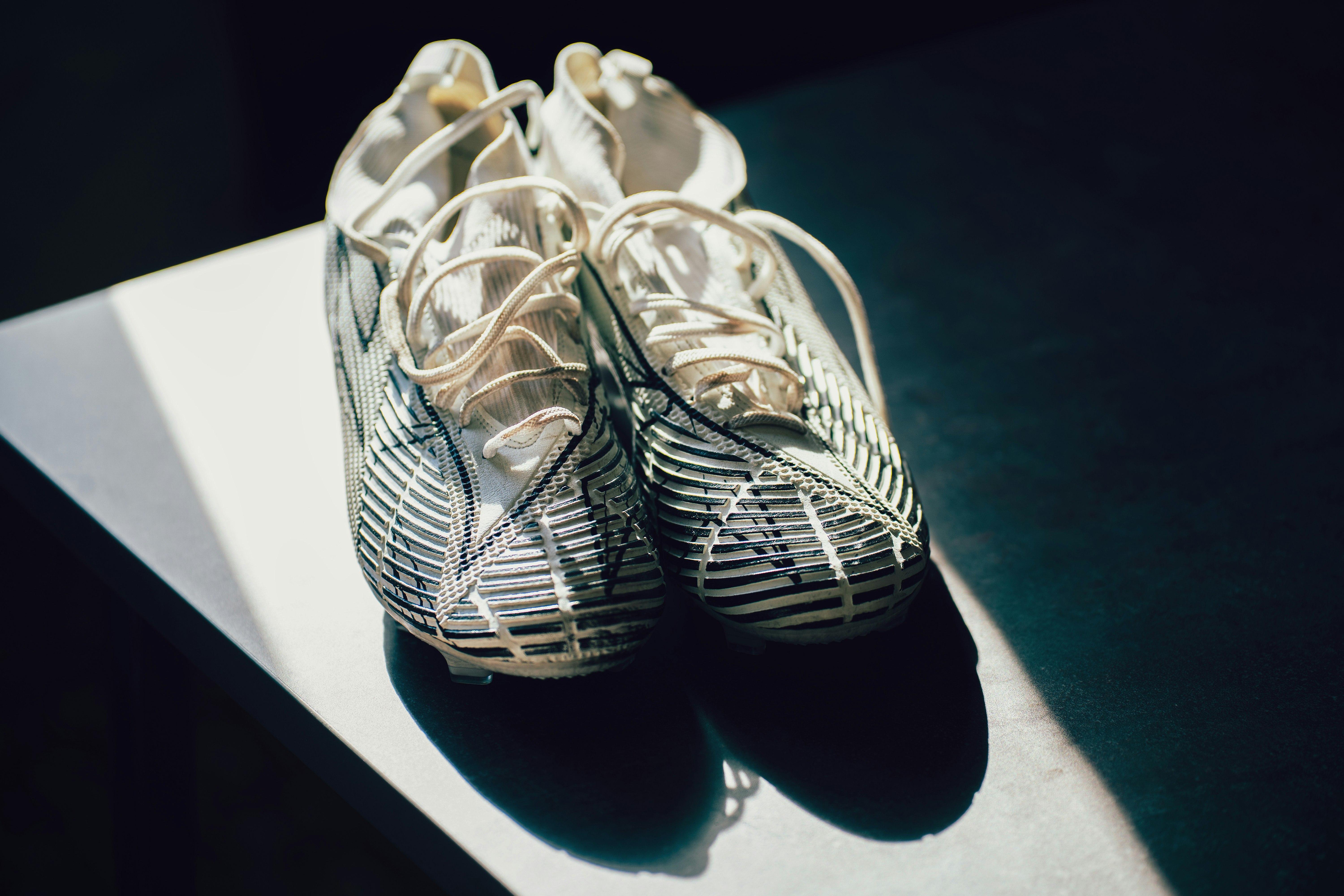 A pair of white soccer cleats with black striped patterns on a table