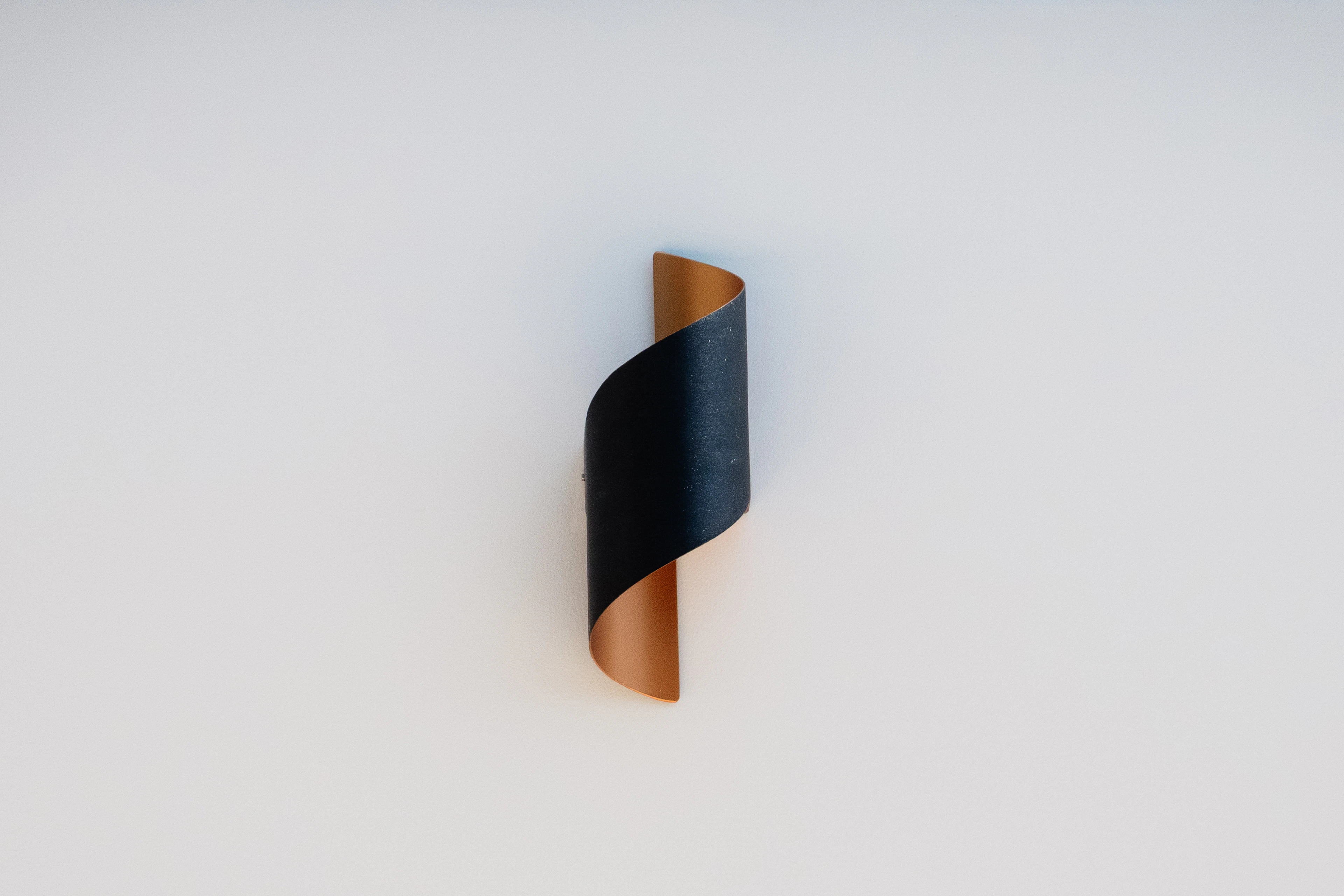 A curved black and gold wall sconce on a plain white wall