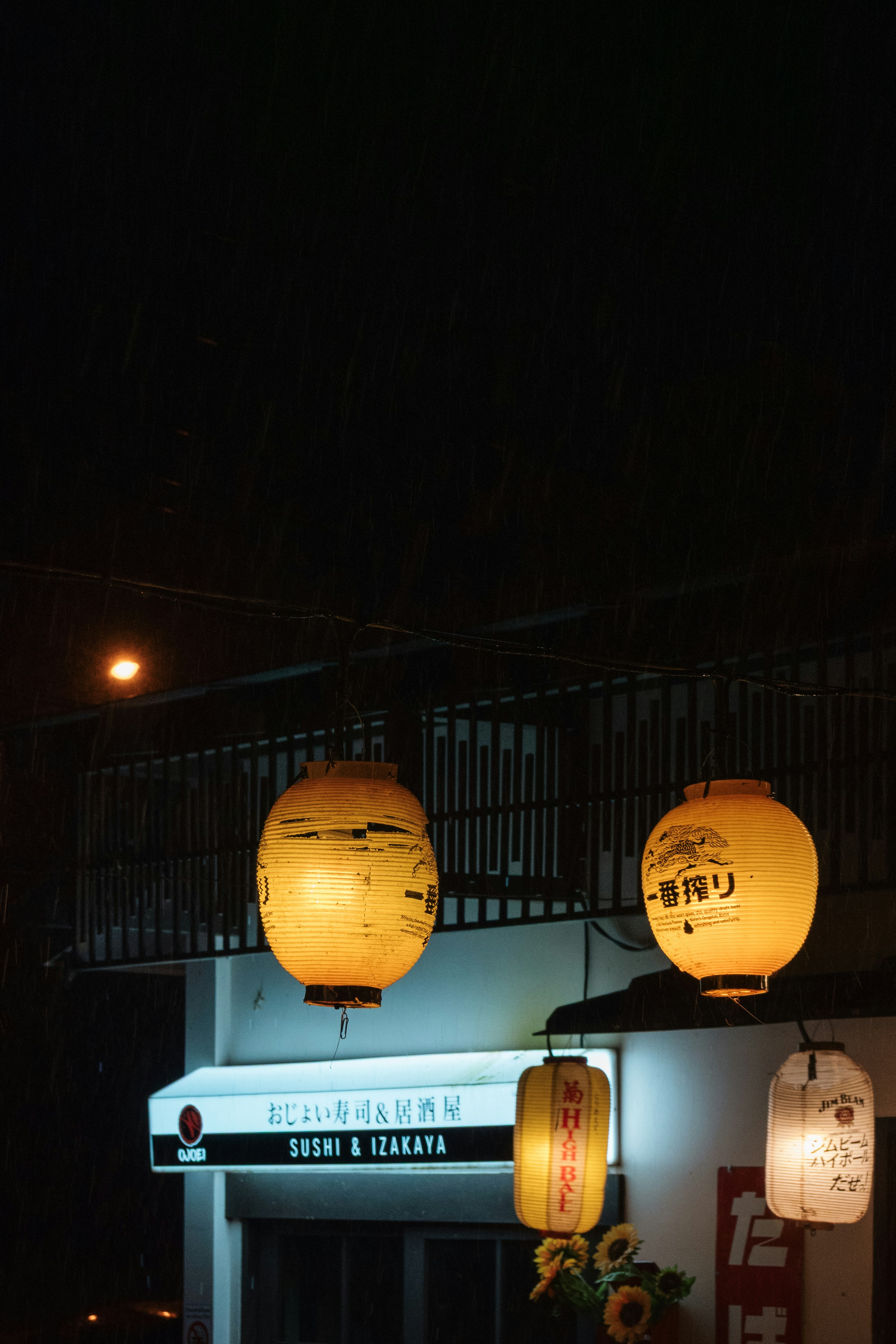 Glowing paper lanterns hanging outside a sushi and izakaya restaurant at night