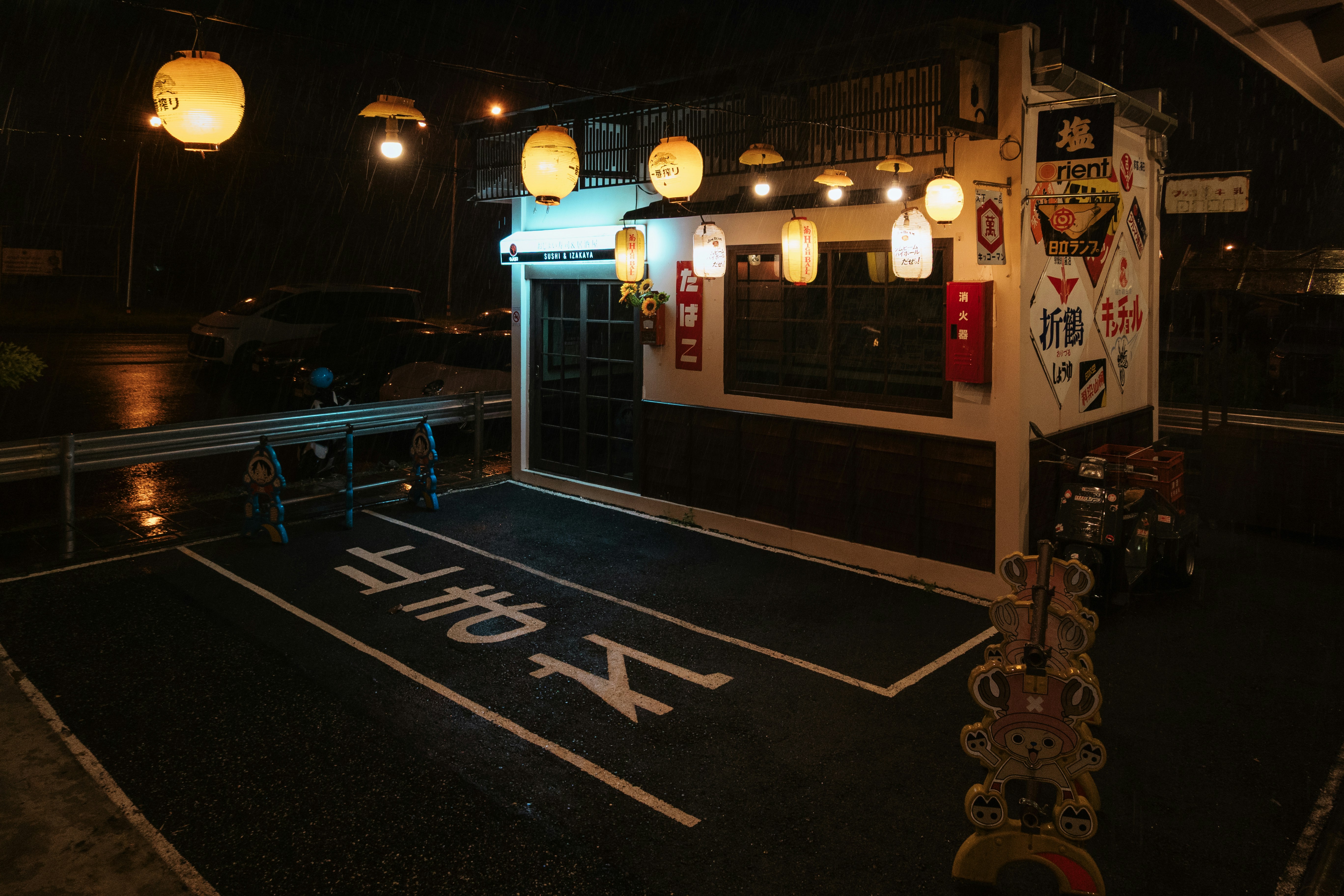 A small sushi and izakaya restaurant illuminated by glowing paper lanterns at night