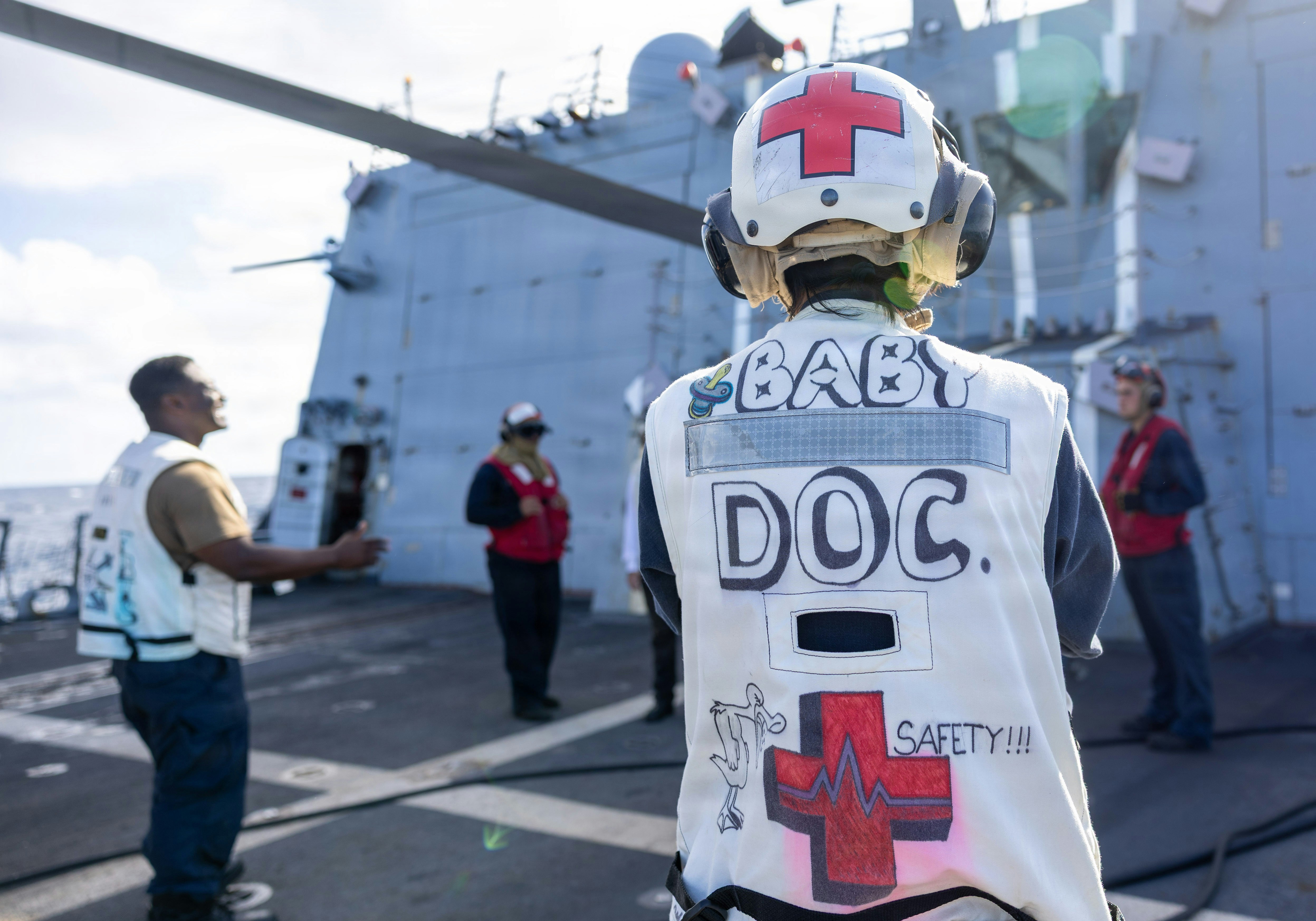 A person wearing a white vest marked Baby Doc on a ship deck