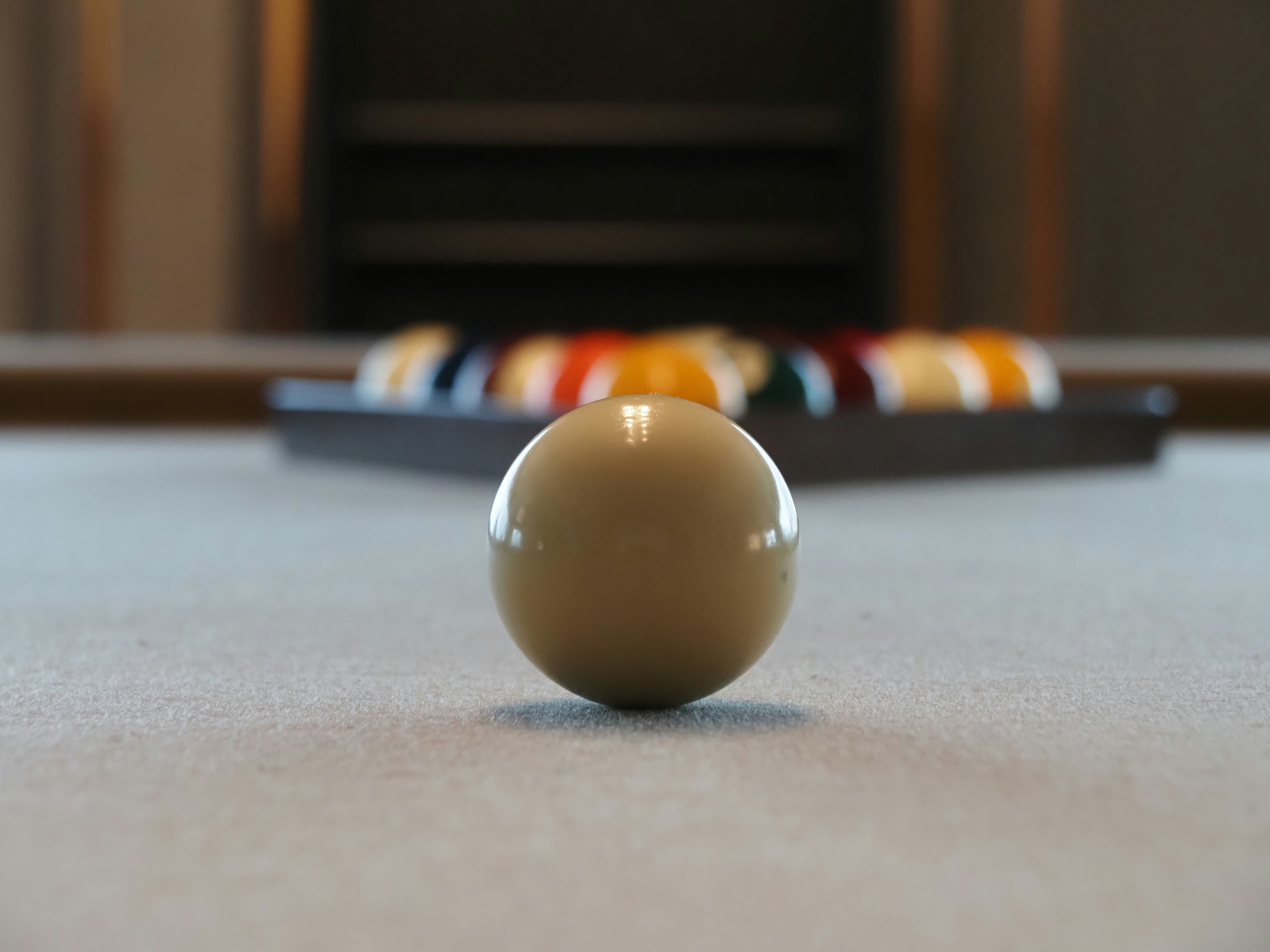 A white cue ball on a pool table with a rack of balls behind