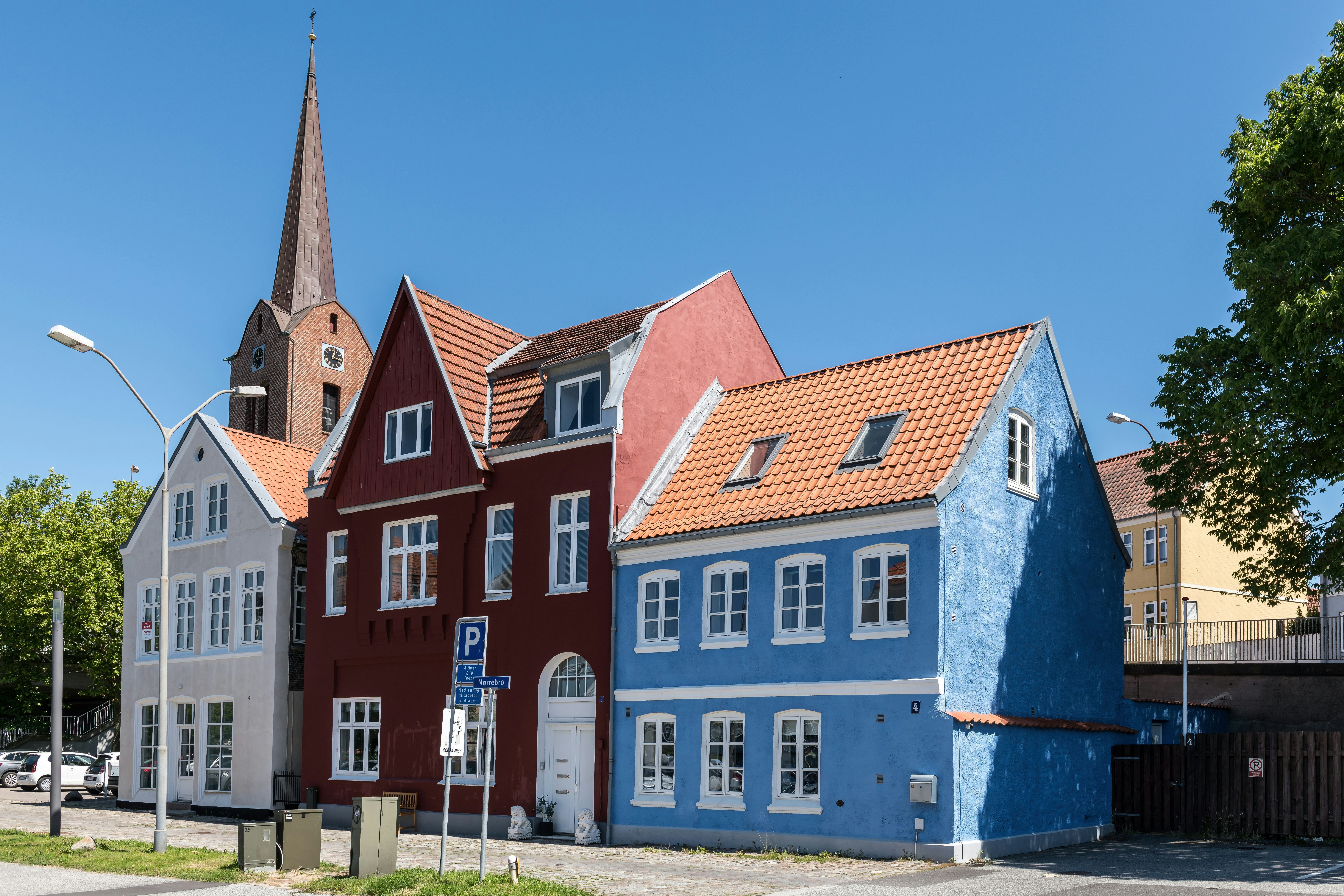 A row of colorful houses with tiled roofs beside a tall church spire