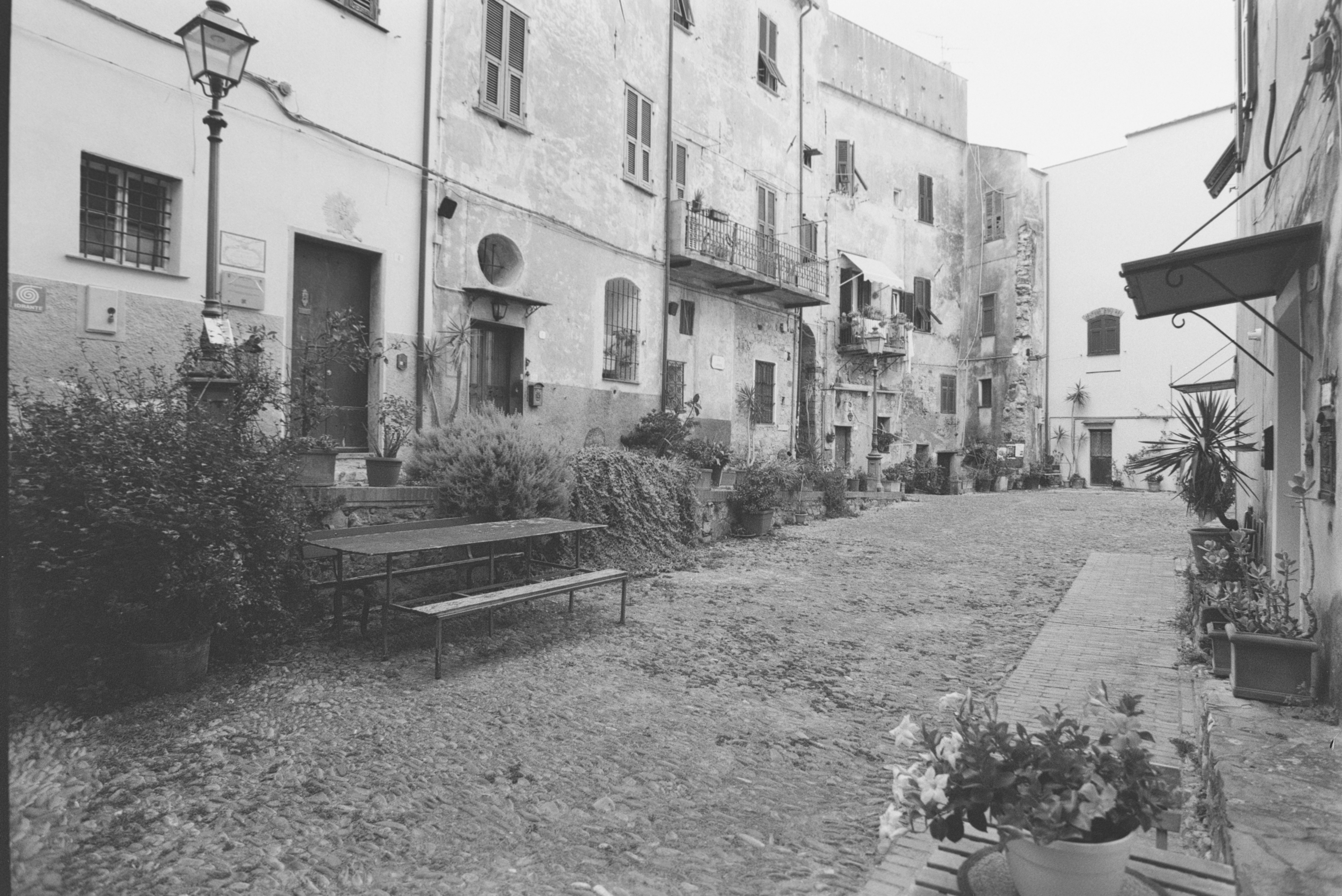 Ein Kopfsteinpflasterhof mit einem Metall-Picknicktisch und Topfpflanzen in einem alten Dorf