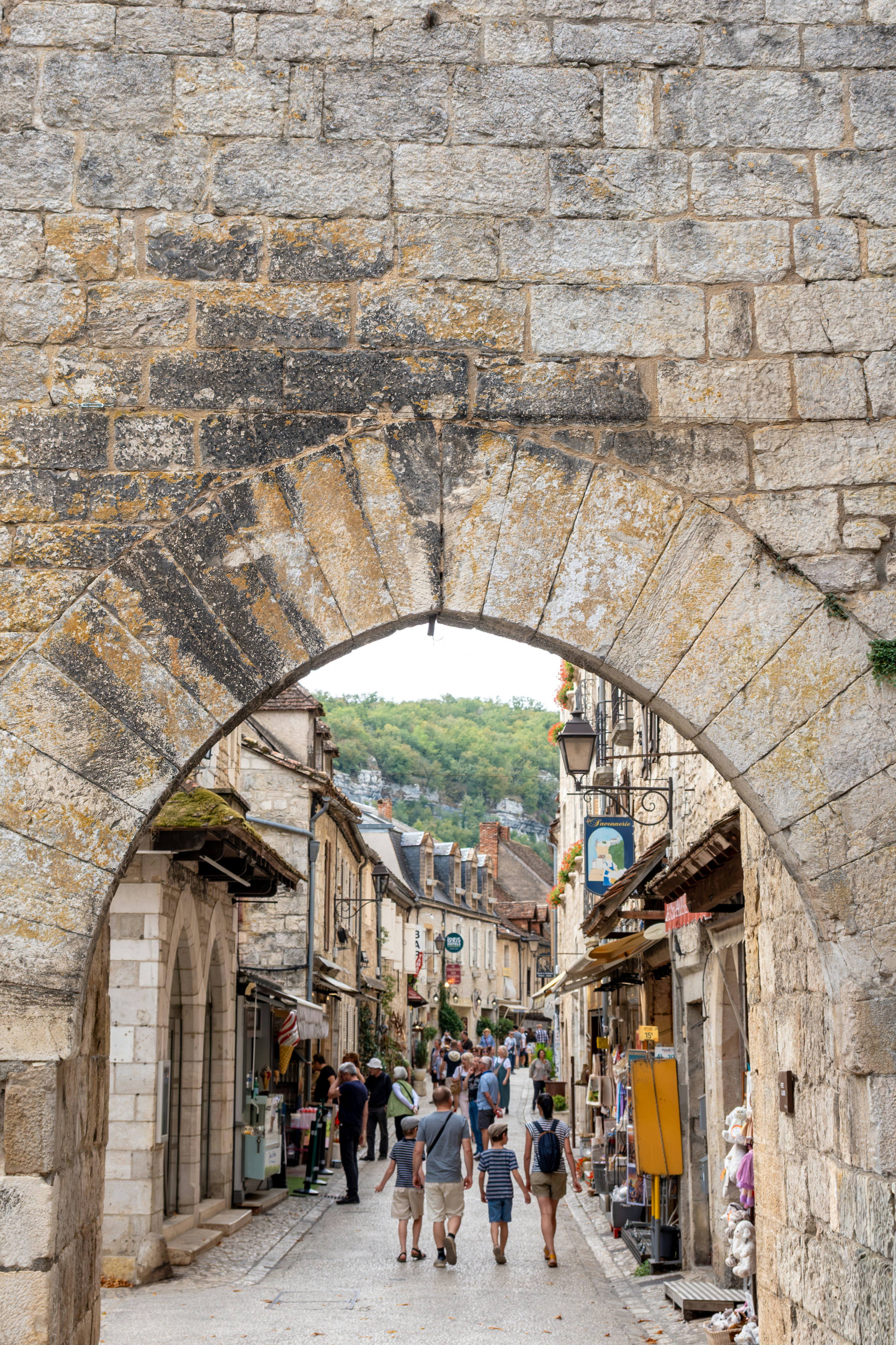 People walking through a stone archway into a narrow street in Saint-Cirq-Lapopie