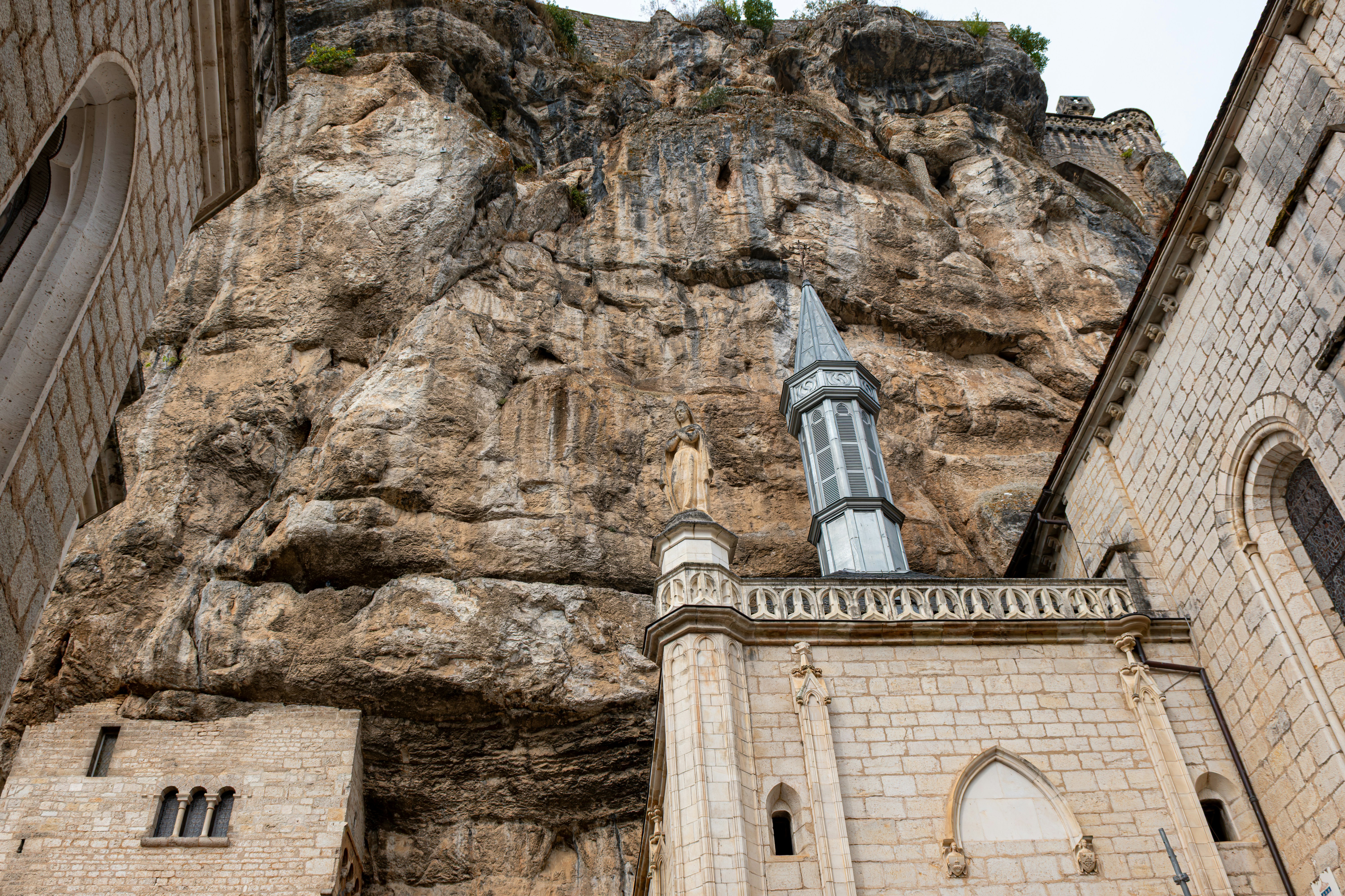 A stone chapel built into a towering cliff face with a statue on top