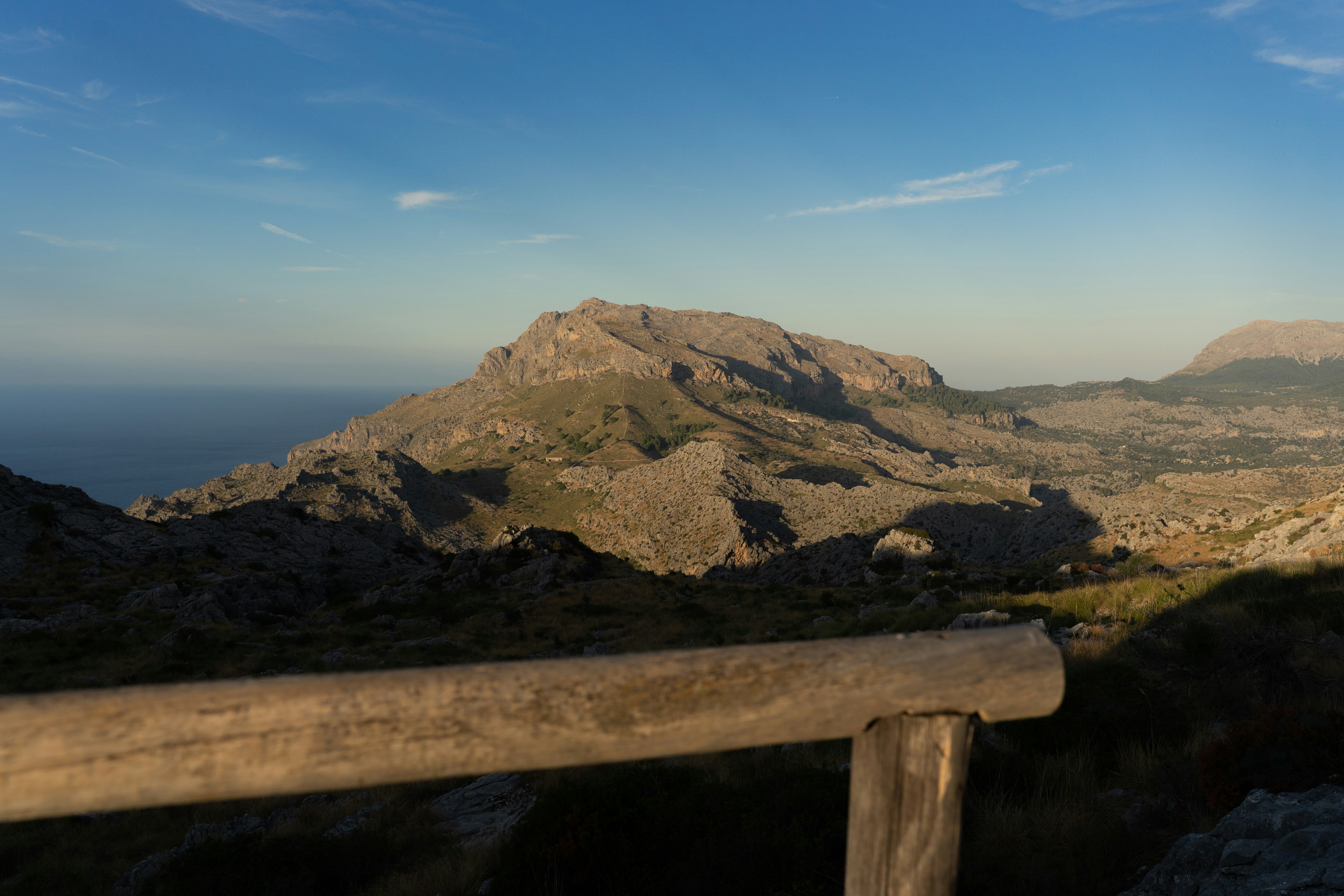 A rocky mountain range under a clear blue sky with a wooden railing