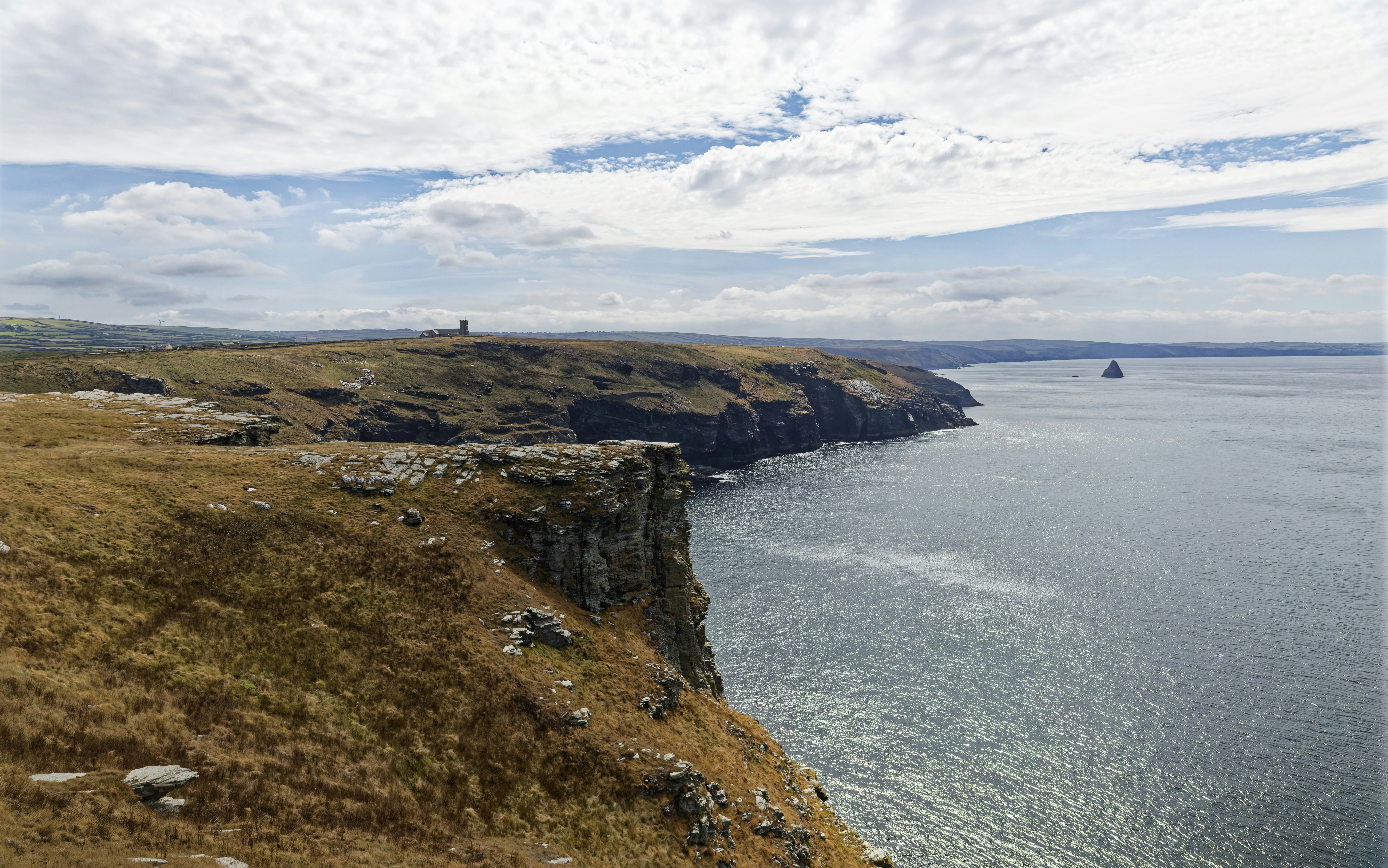 Rugged cliffs overlooking the sea under a bright sky with scattered clouds