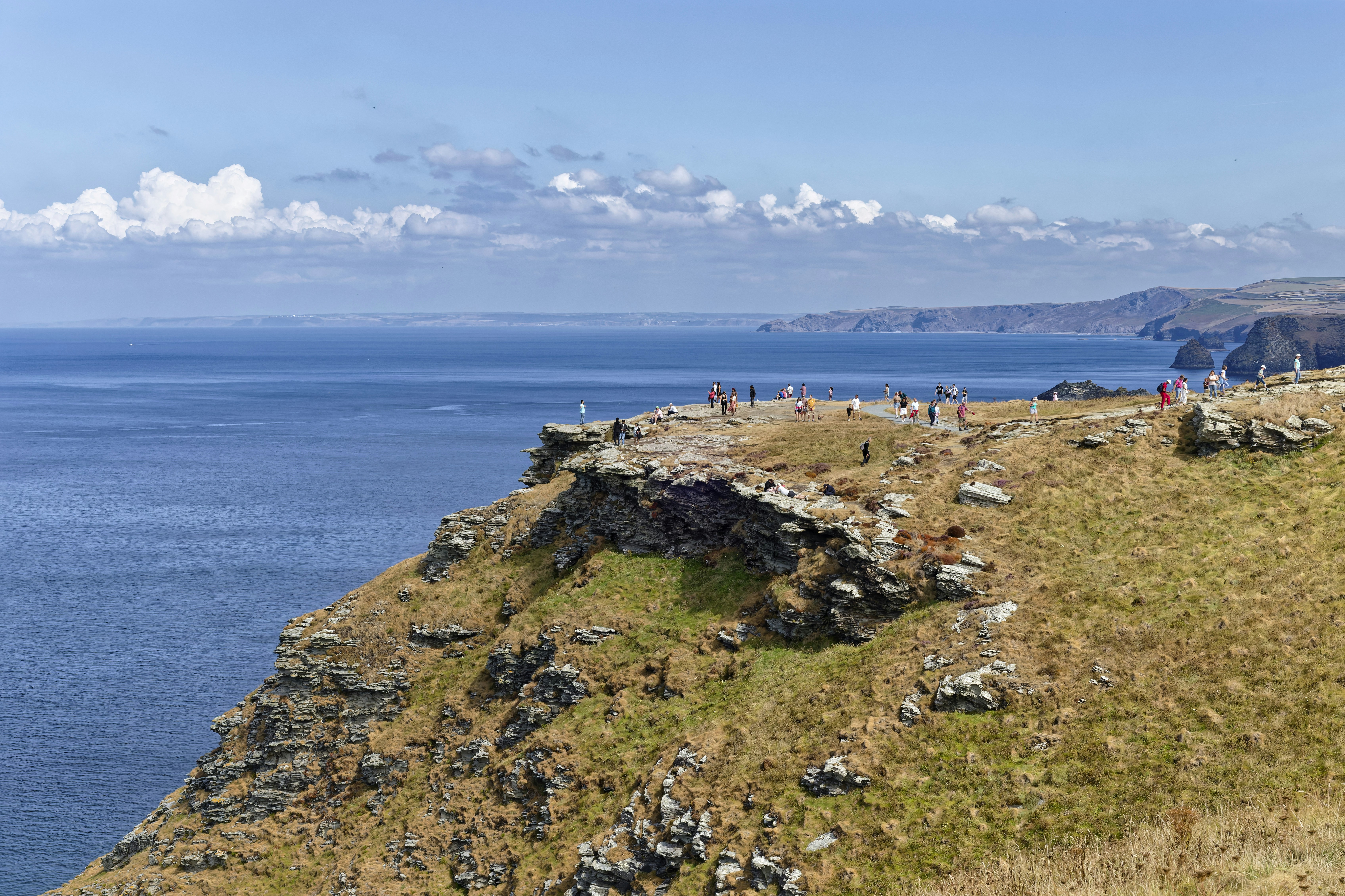 A group of people walking on a rocky cliff edge above the ocean