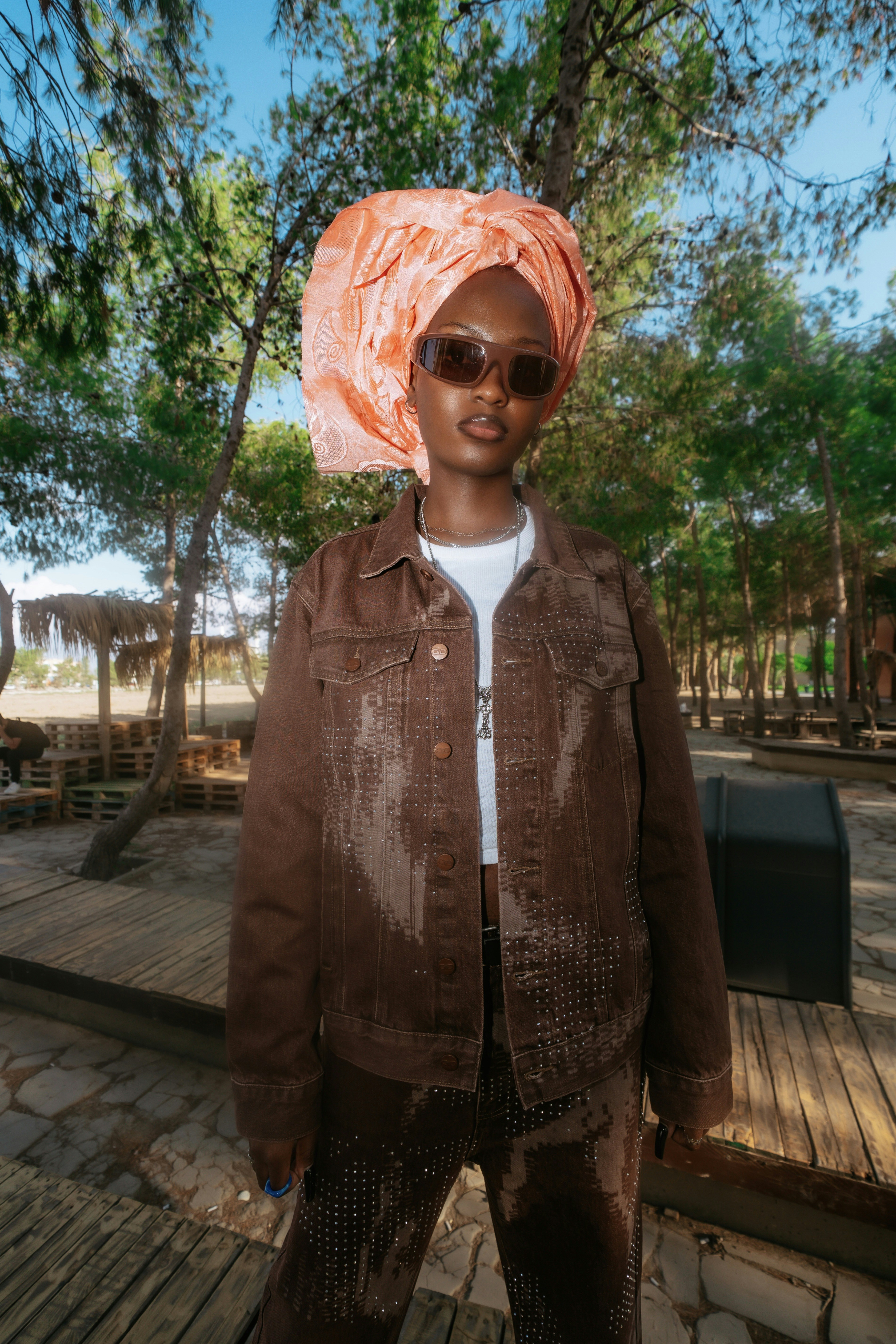 A woman in a brown denim jacket and headwrap standing in a pine forest