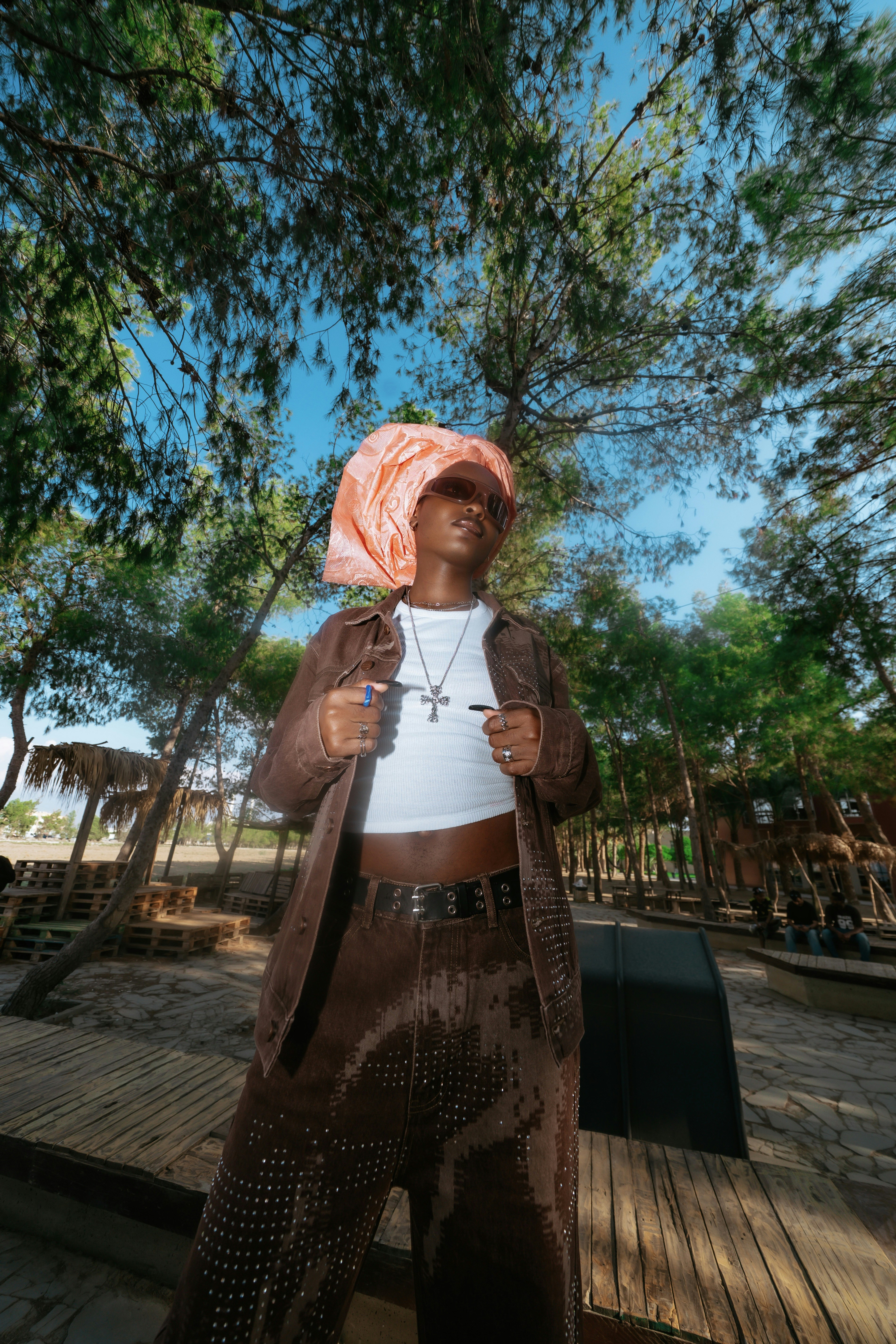 A person in a brown denim outfit and peach headwrap standing in a forest