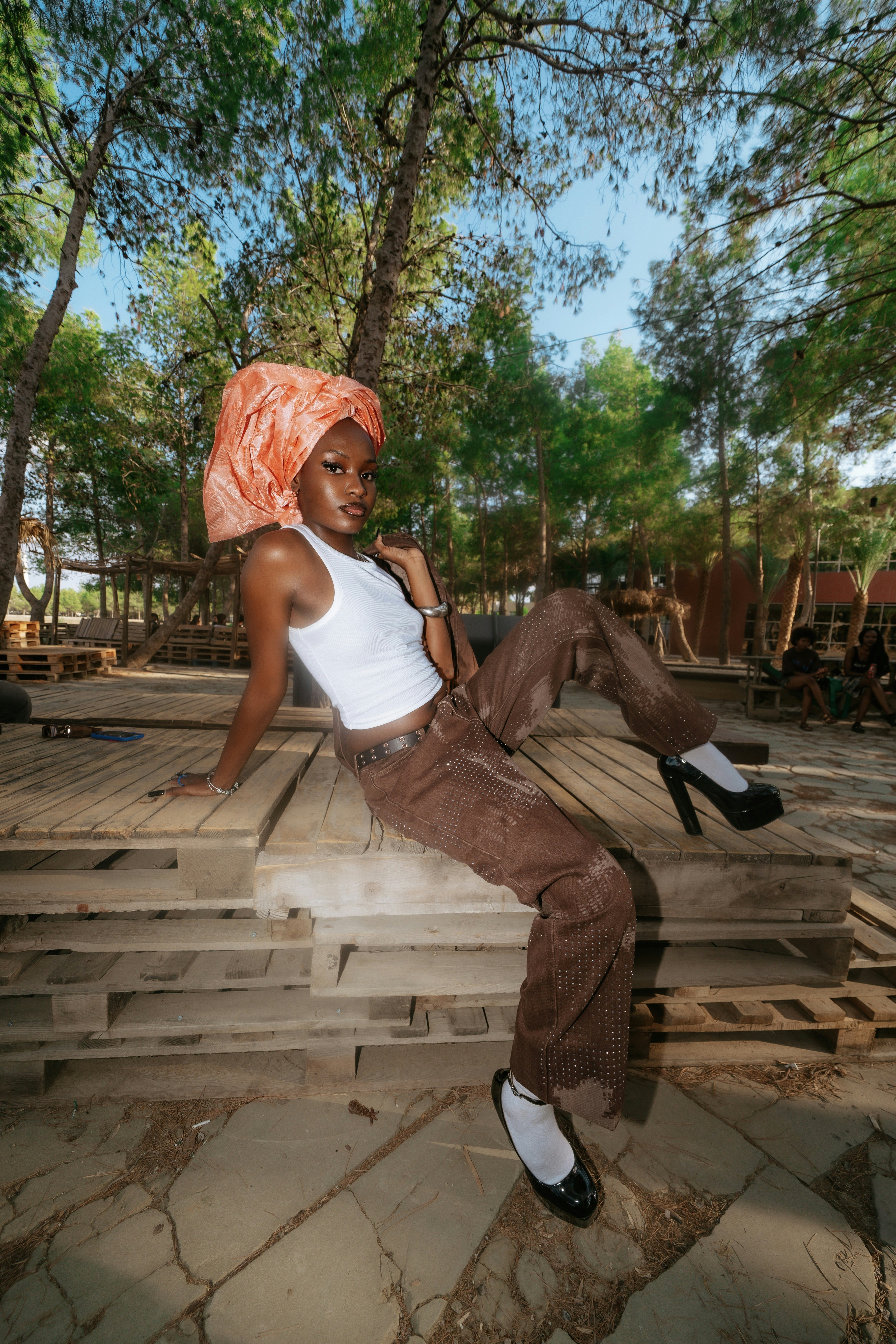 A woman in a white tank top and brown pants sitting on wooden pallets