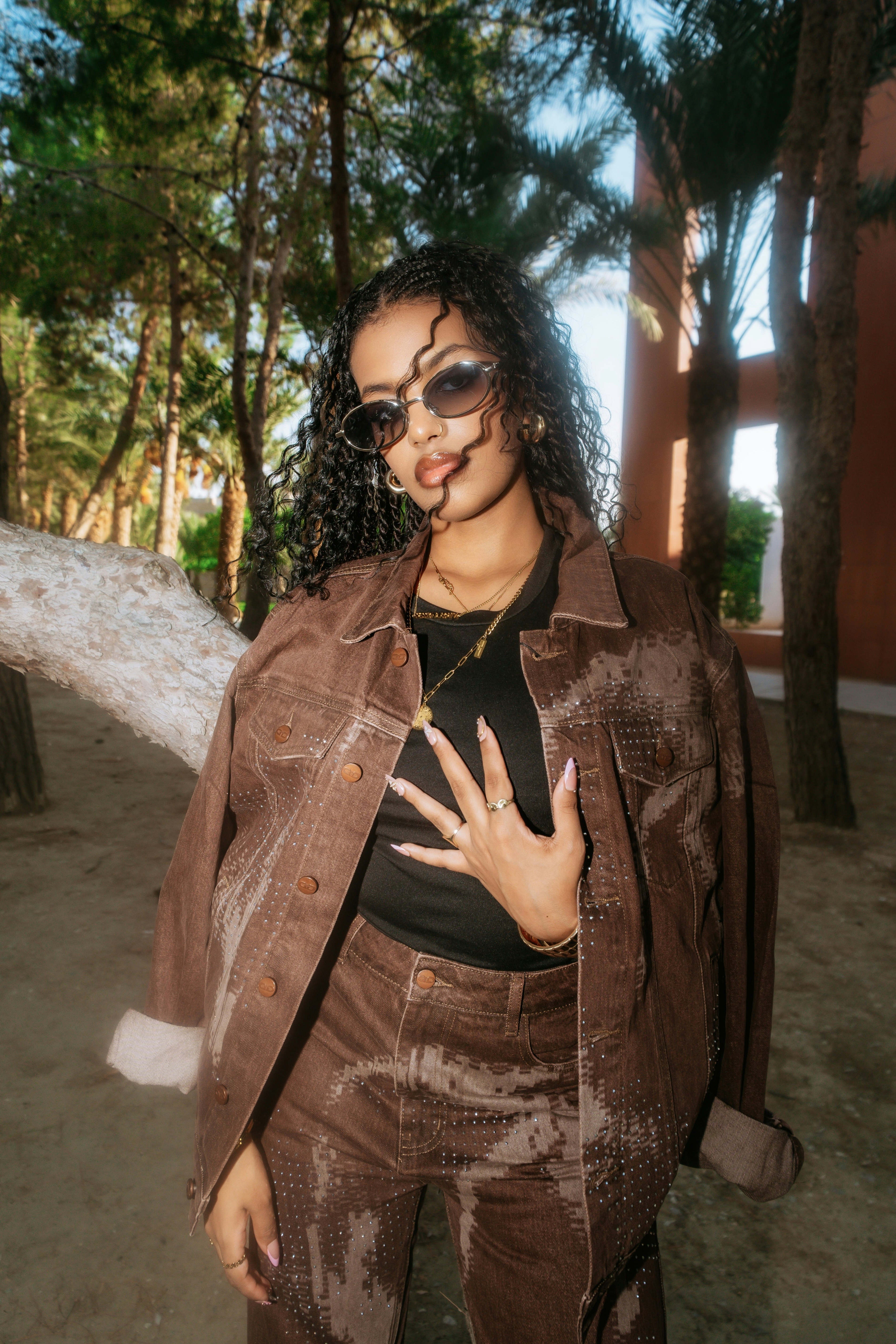 A woman in a brown denim jacket and pants among palm trees