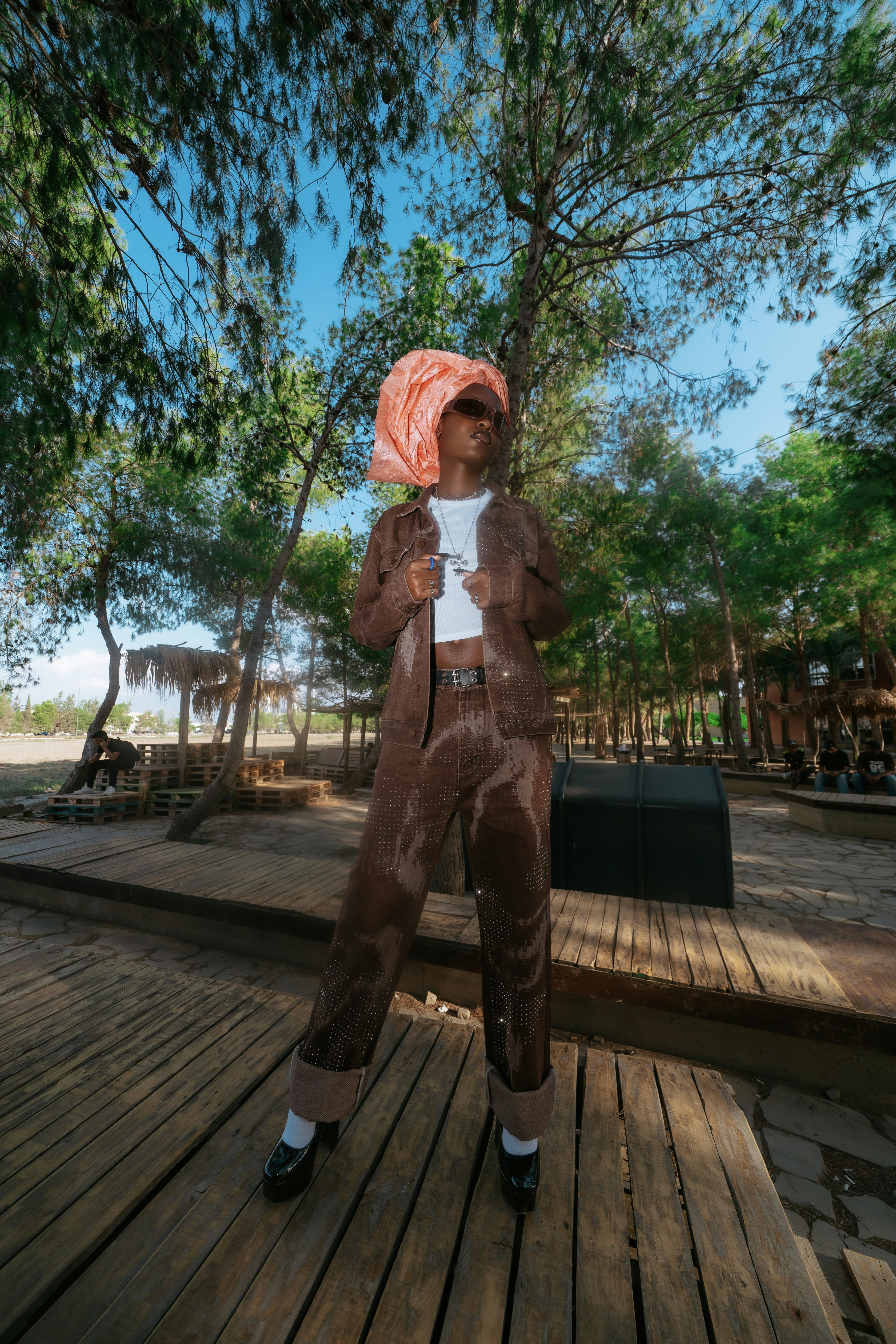 A person in a brown denim outfit and peach headwrap on a wooden deck