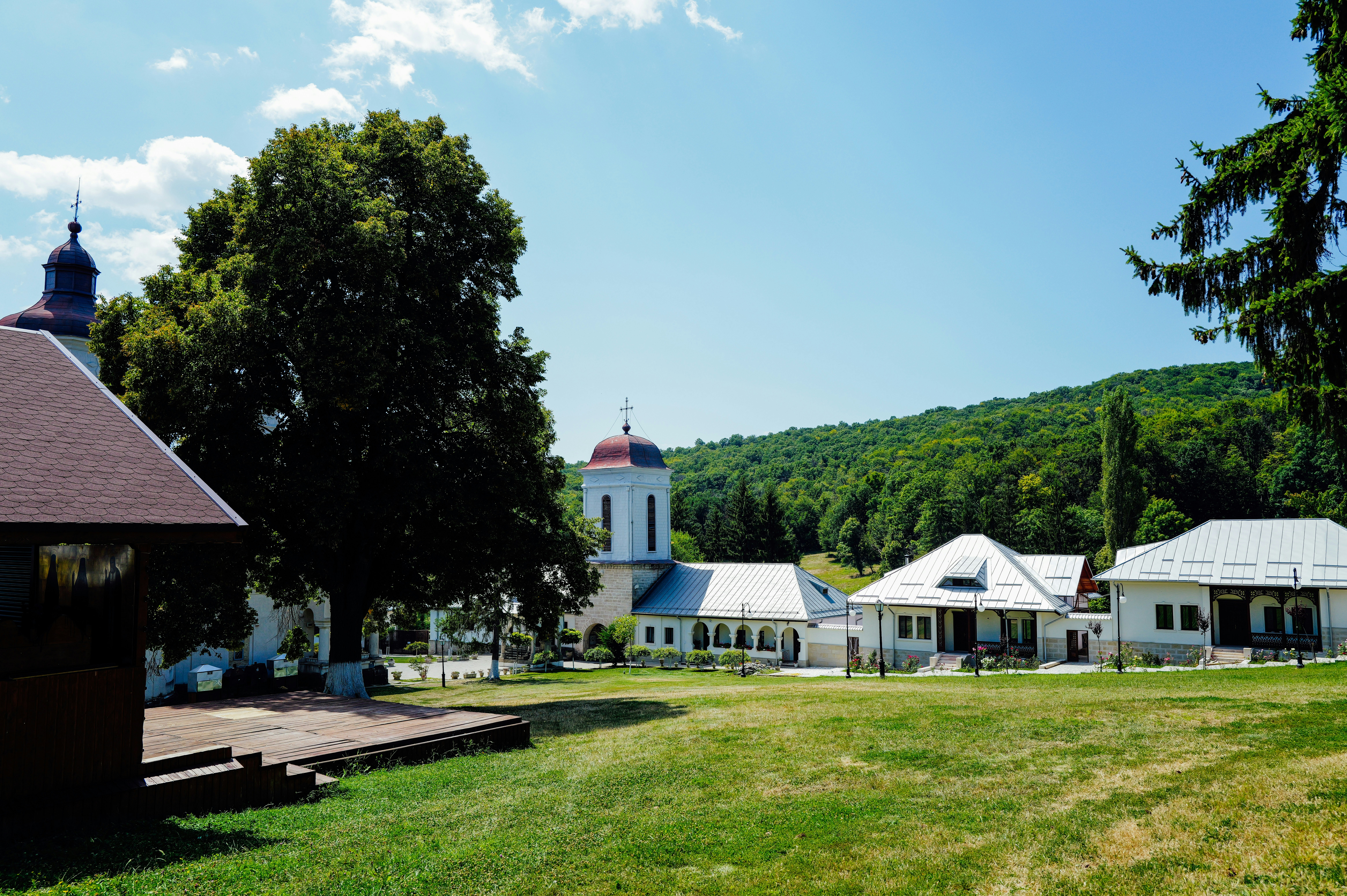 White monastery buildings with metal roofs on a grassy hill under a blue sky