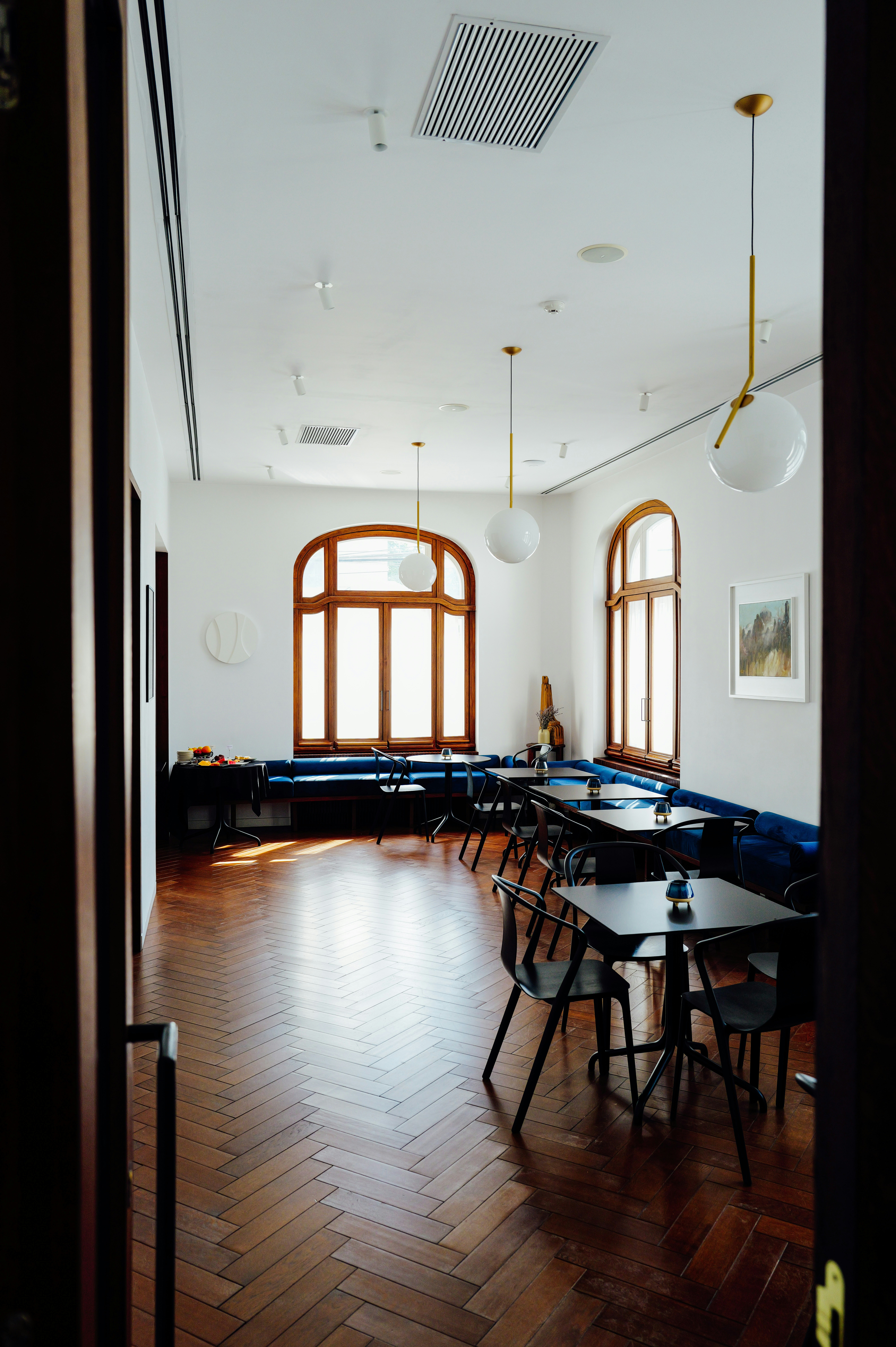A restaurant interior with dark wooden floors, blue velvet benches, and modern globe pendant lights