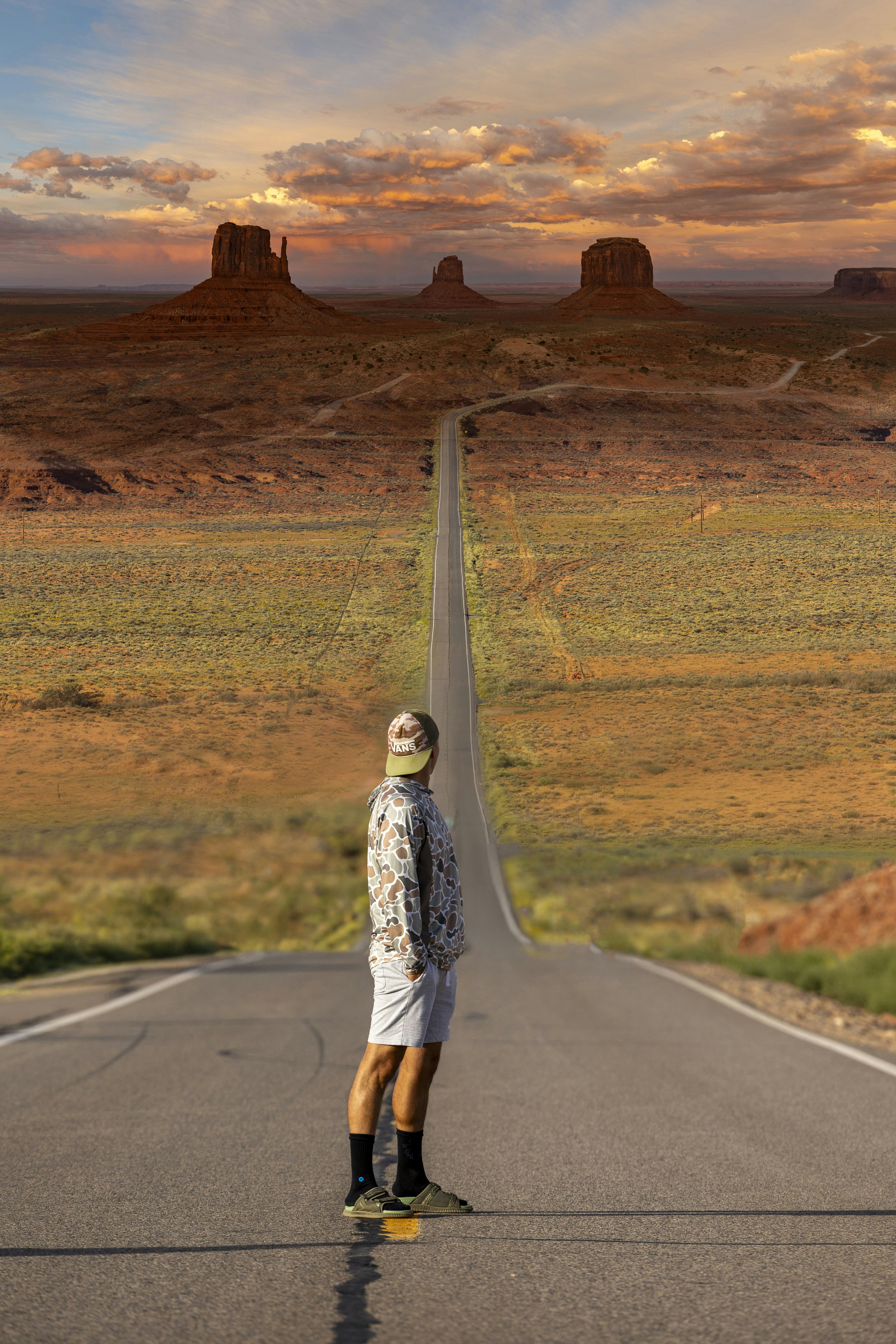 A person in a camouflage hoodie and cap on a road in Monument Valley