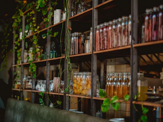 Glass jars and bottles on wooden shelves with trailing green plants in a cafe