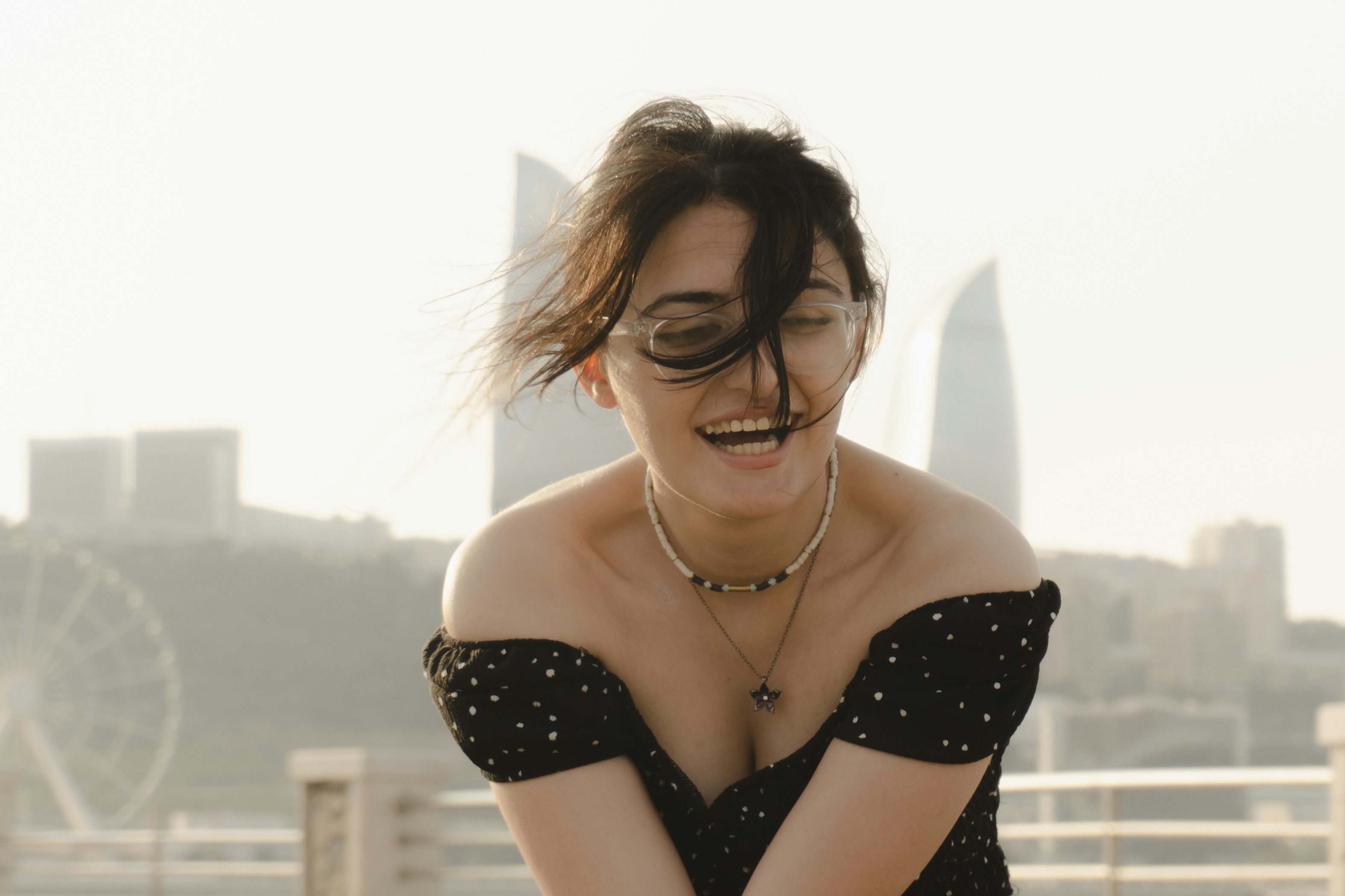 A laughing woman with windblown hair wearing glasses and a polka dot top